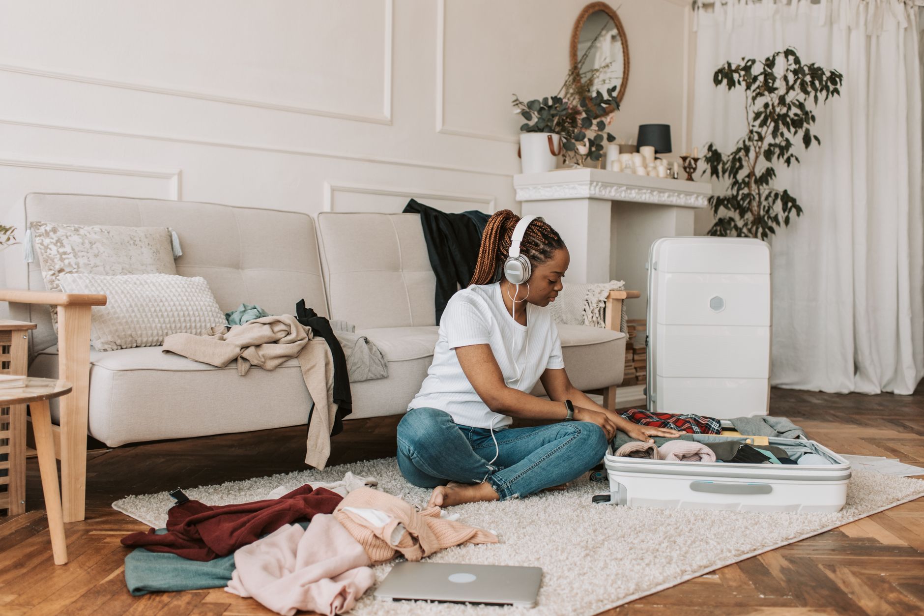 Woman packing an open suitcase with folded clothes in a cozy living room.