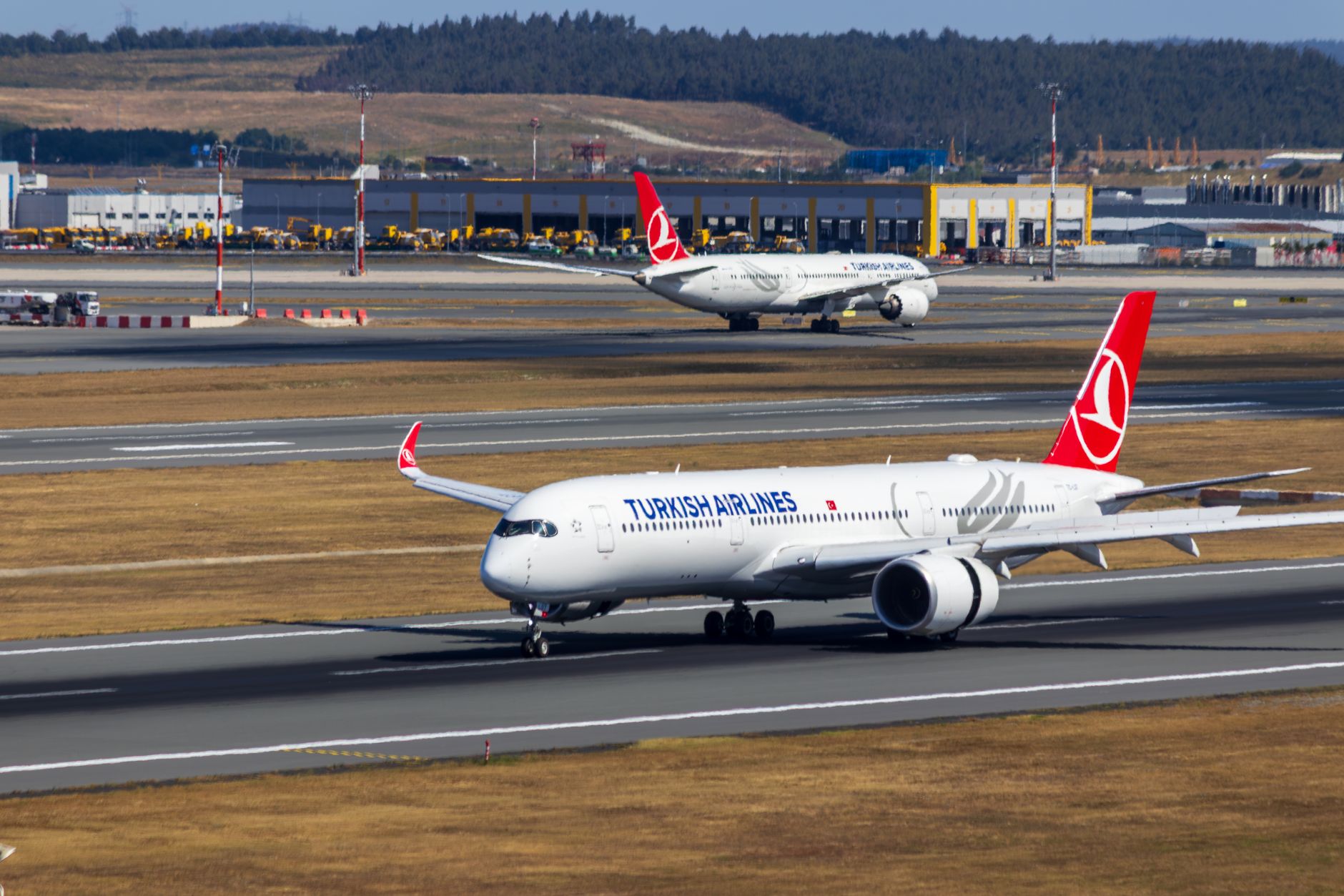 Two Turkish Airlines planes on the runway at an airport, showcasing busy air traffic.