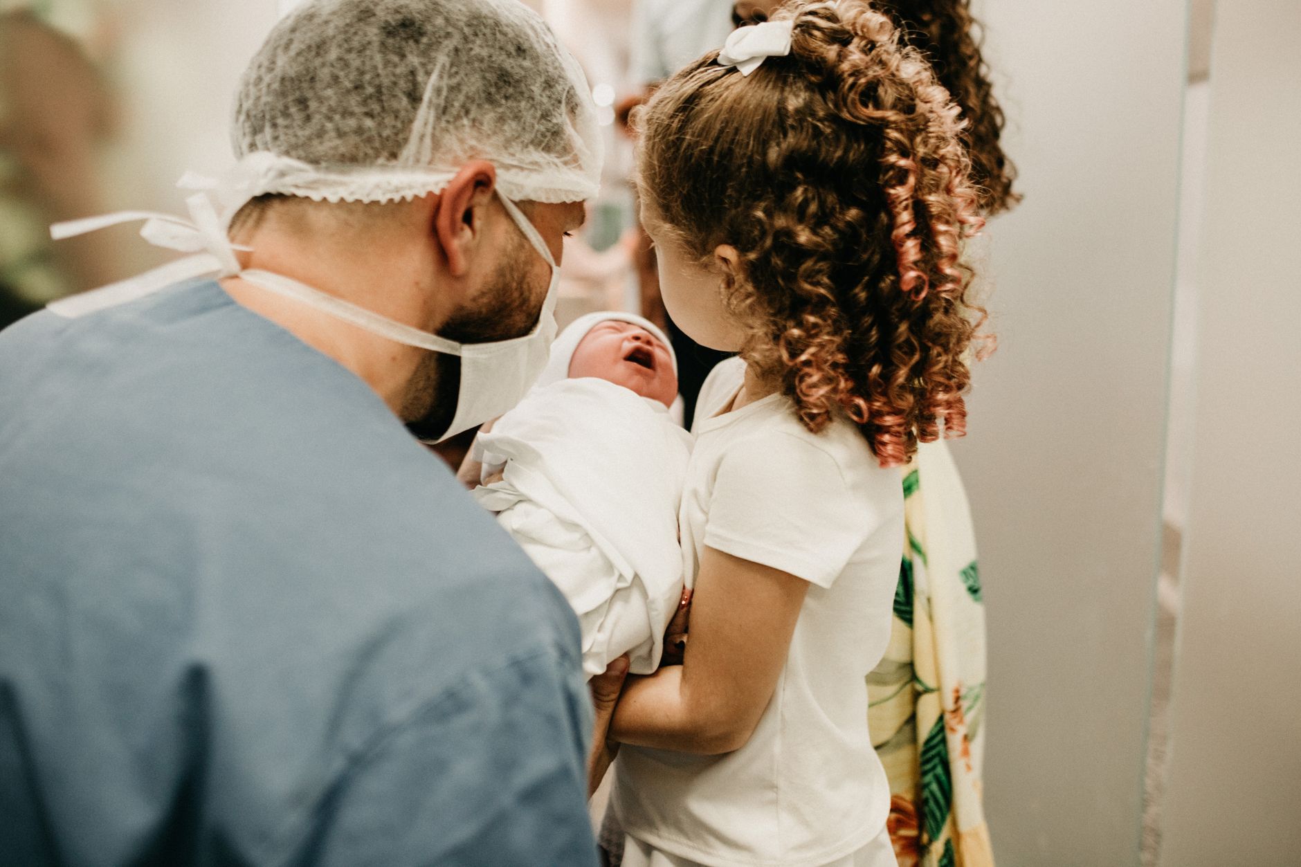 A young girl gently holds her newborn sibling in a hospital room.