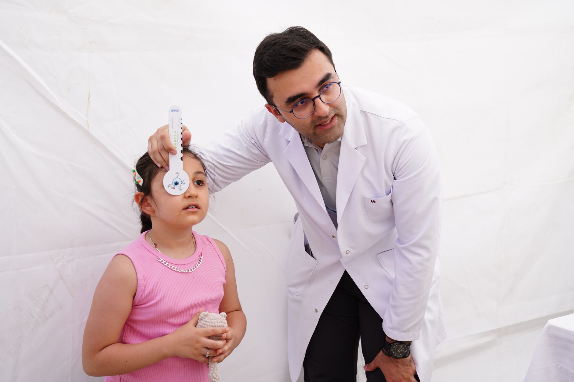 A Turkish haematologist examines a young girl in a medical setting using a measuring device.