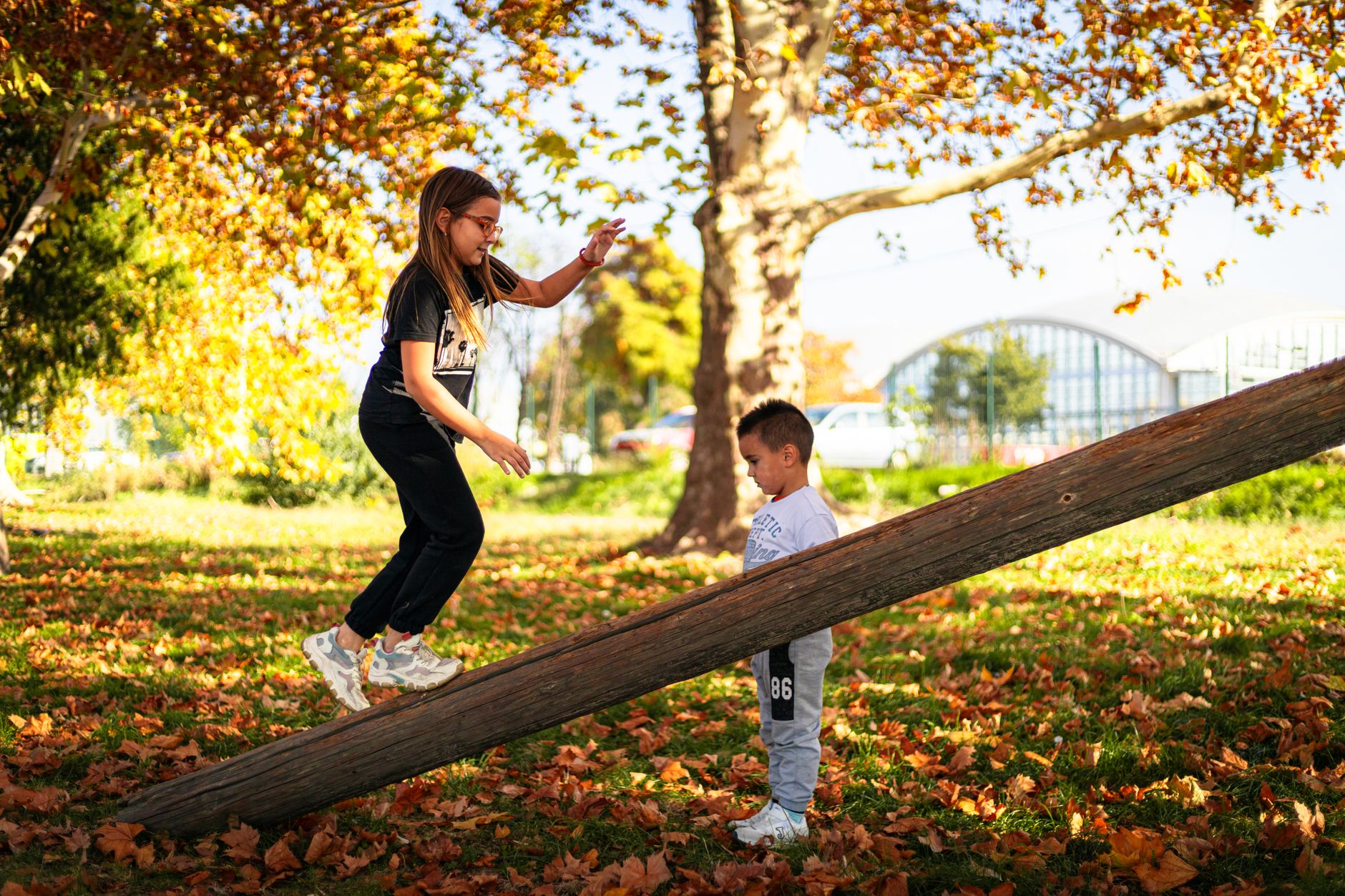 A girl balances on a log while her brother looks on in a colorful park in Istanbul.