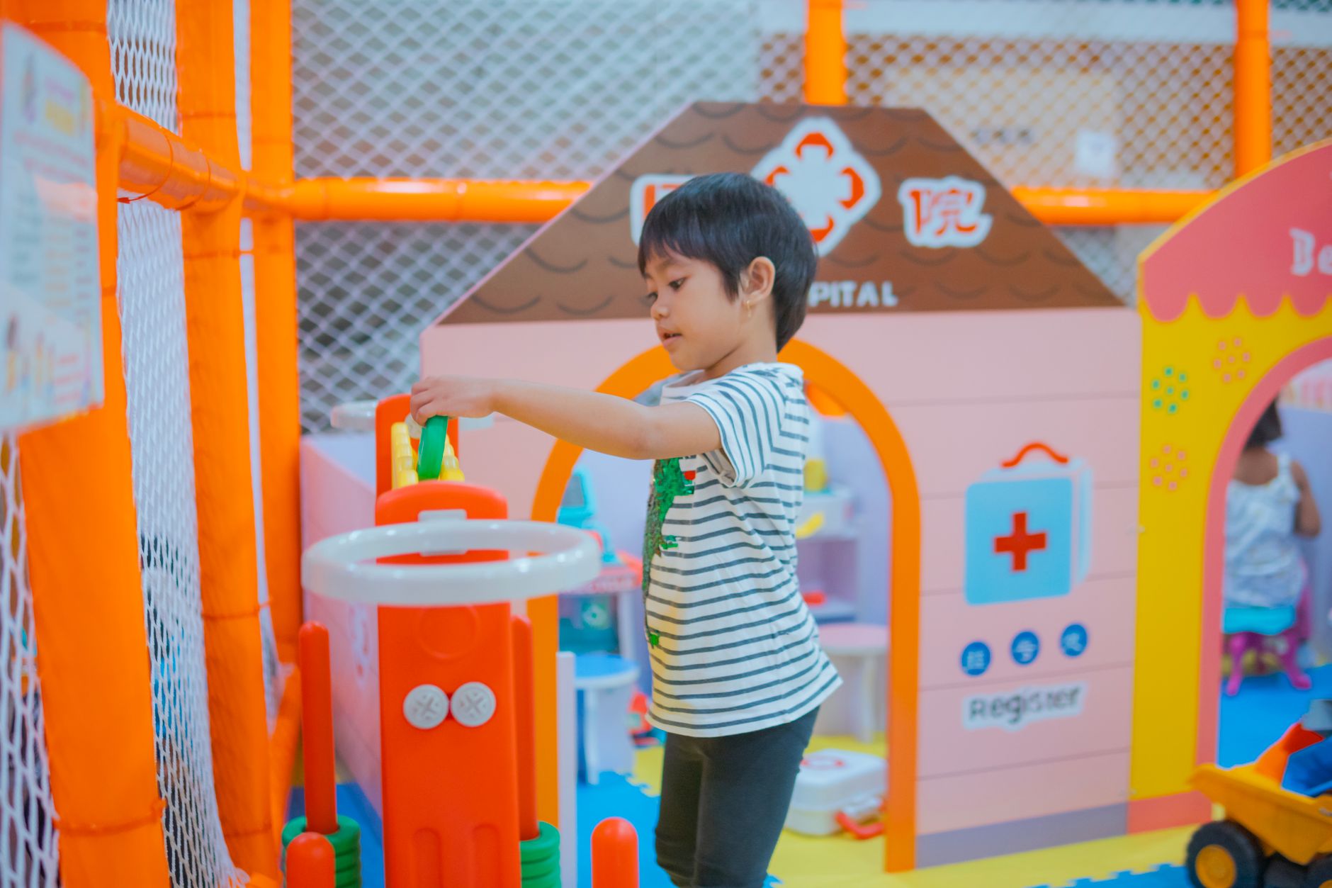 Young child interacting with toy medical equipment in a vibrant play area.