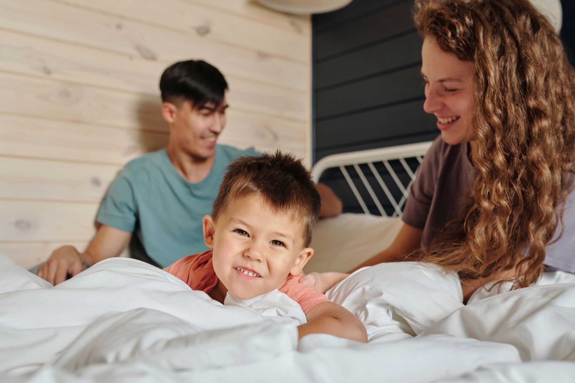 A happy child smiles while playing in bed with parents in a cozy room.