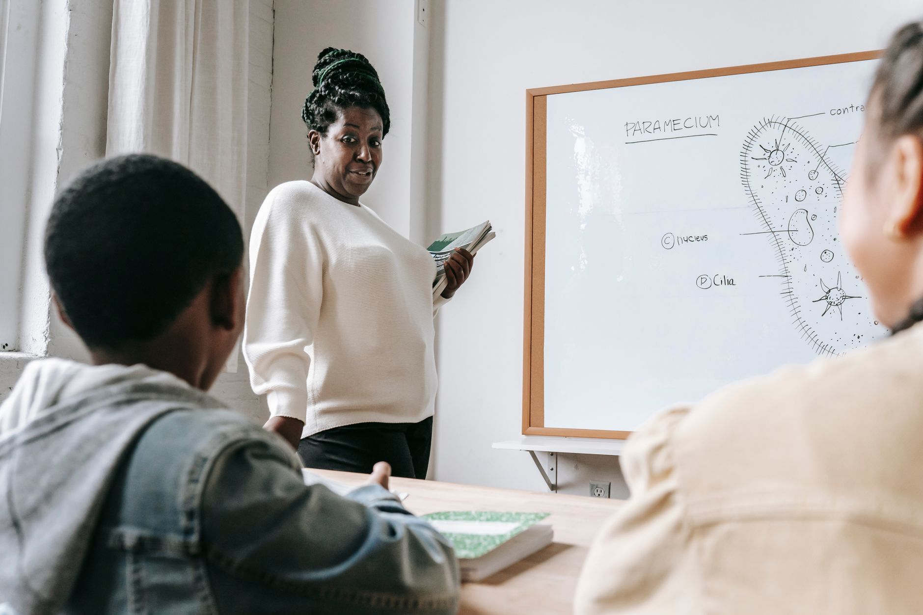 A teacher instructs students on Paramecium anatomy in a bright classroom.
