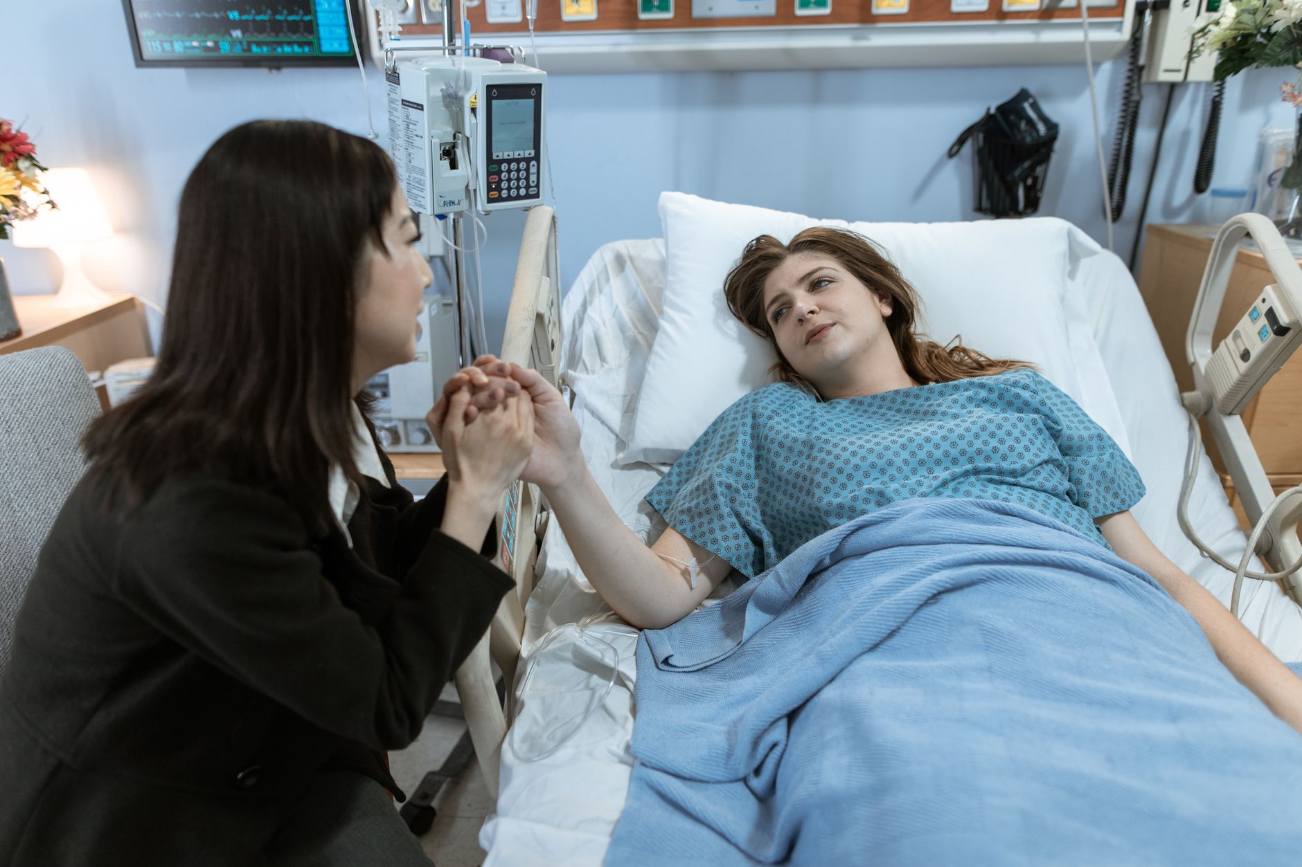 A woman holding the hand of a patient in a hospital bed, showing care in a family-centered recovery room.