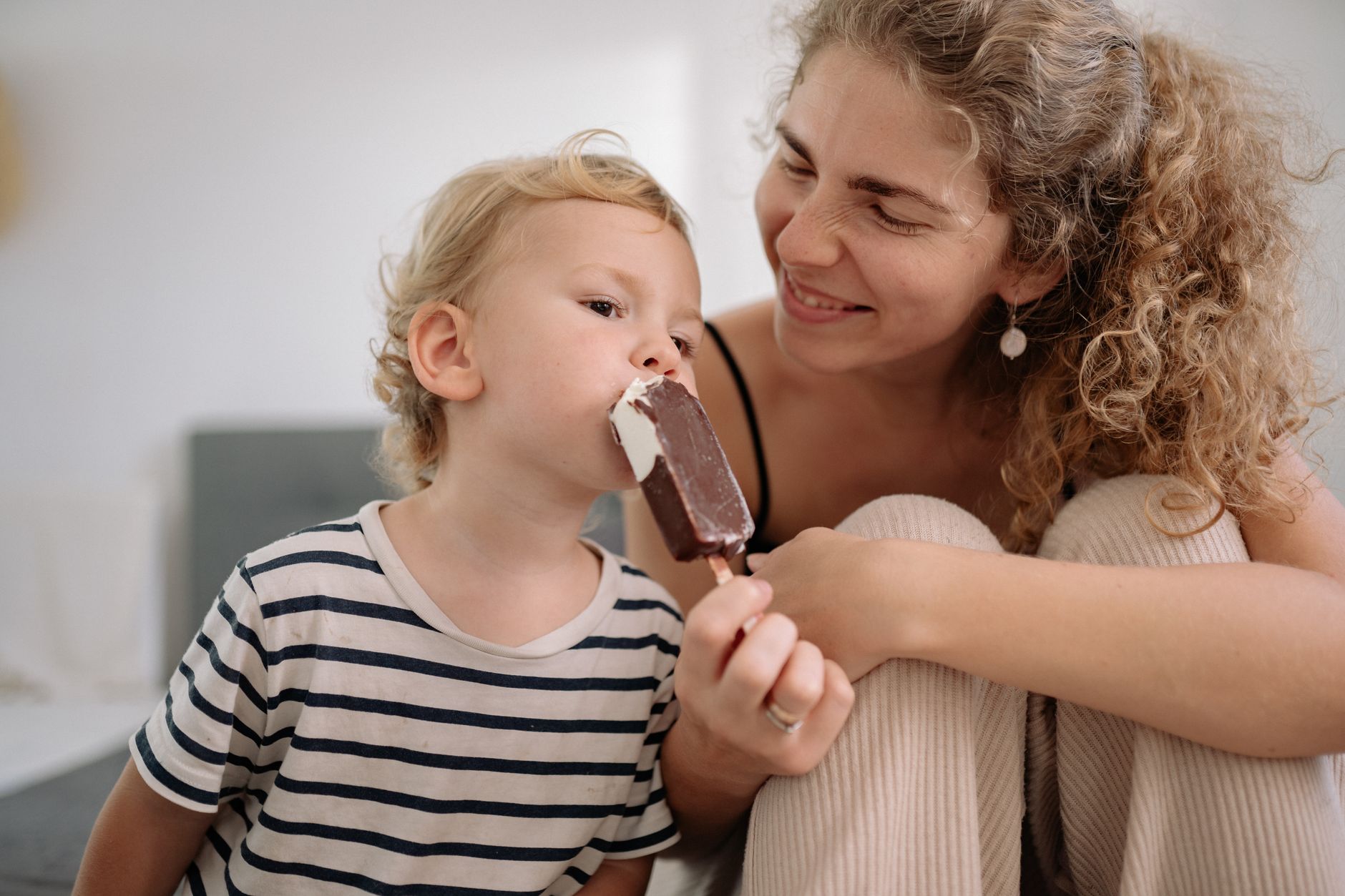 A young child happily eating an ice cream bar with a smiling woman, showcasing a gentle recovery.