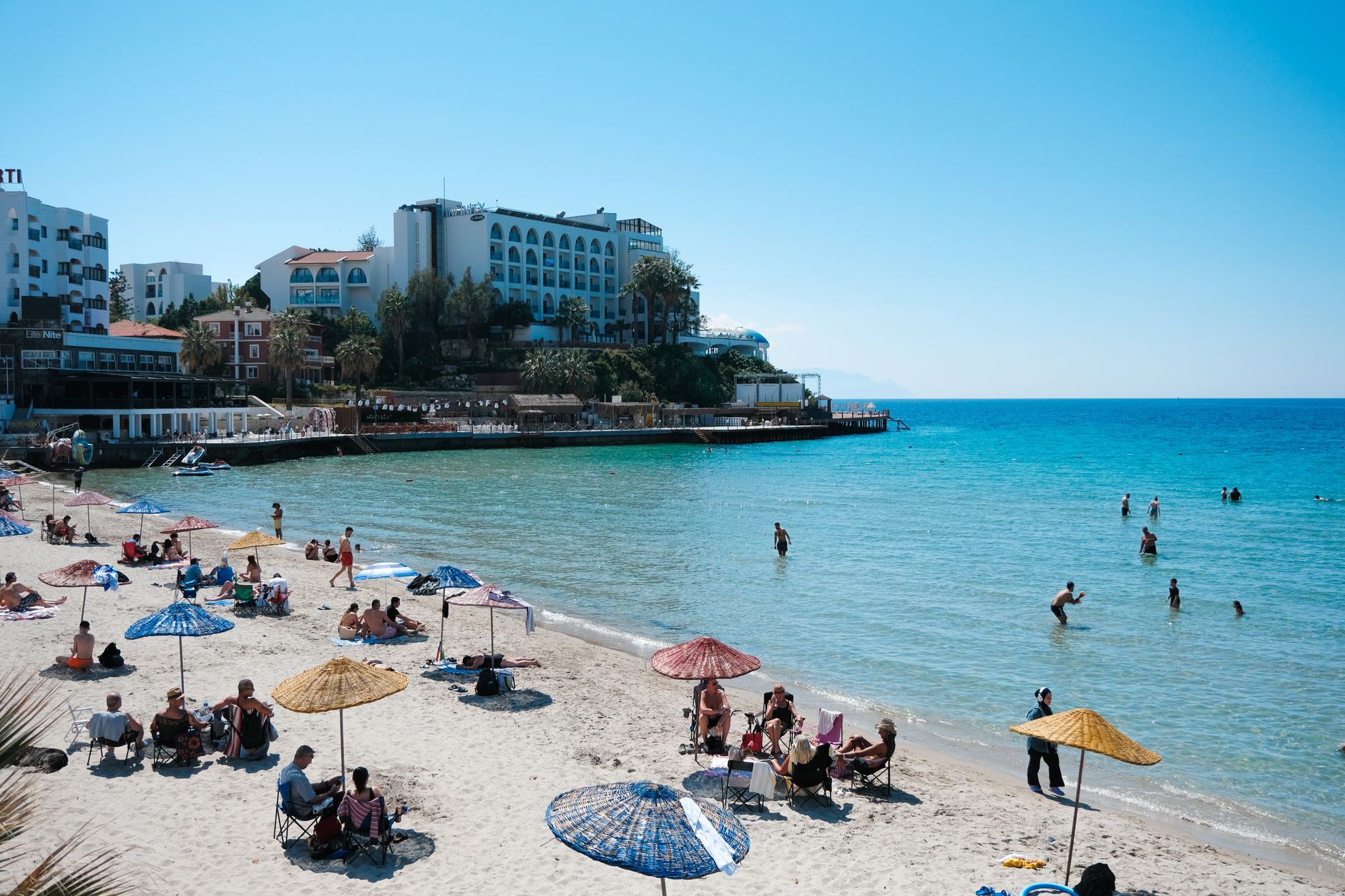 A vibrant Antalya beach scene with sunbathers, umbrellas, and calm waters.