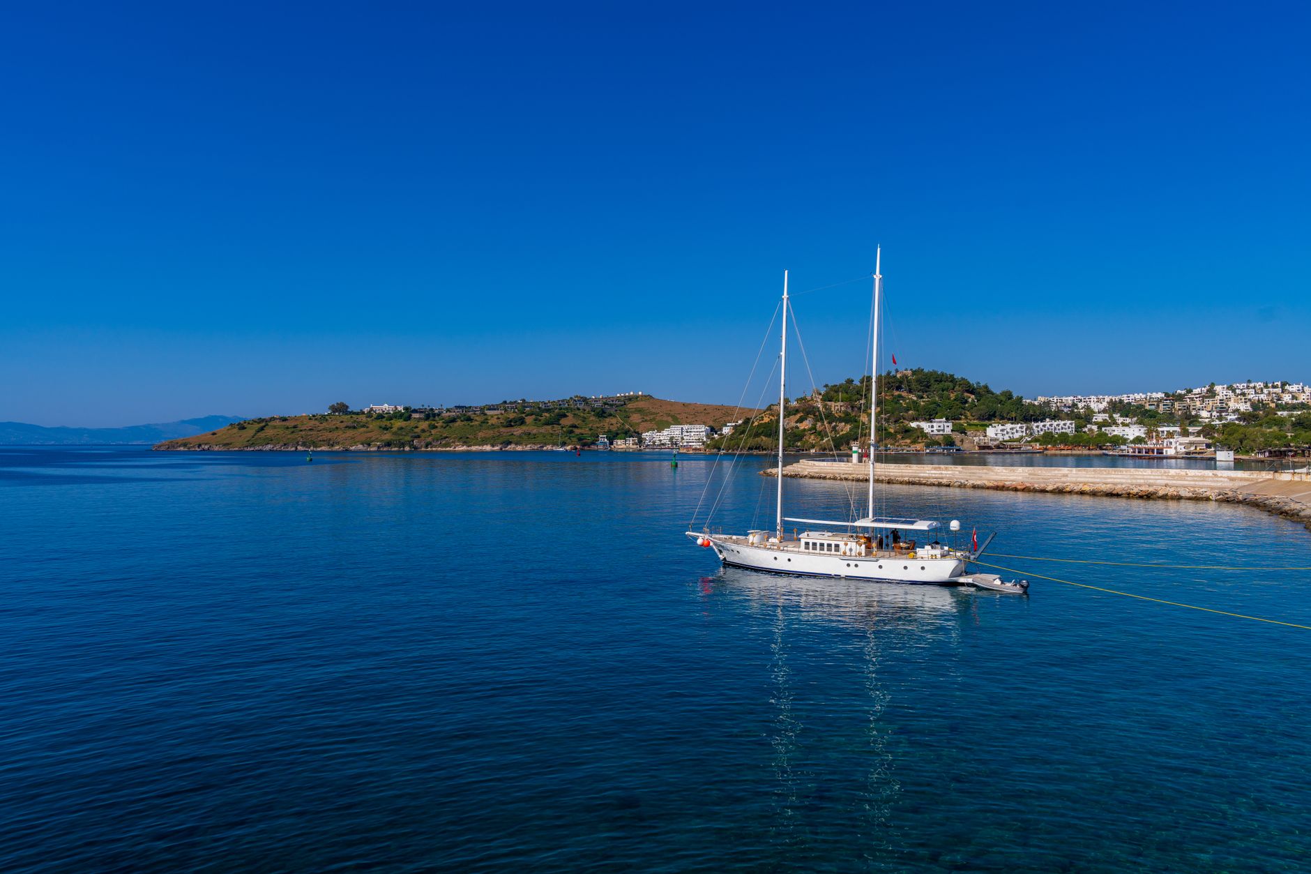 A picturesque view of a calm Bodrum coastline featuring a sailing yacht anchored in serene waters.