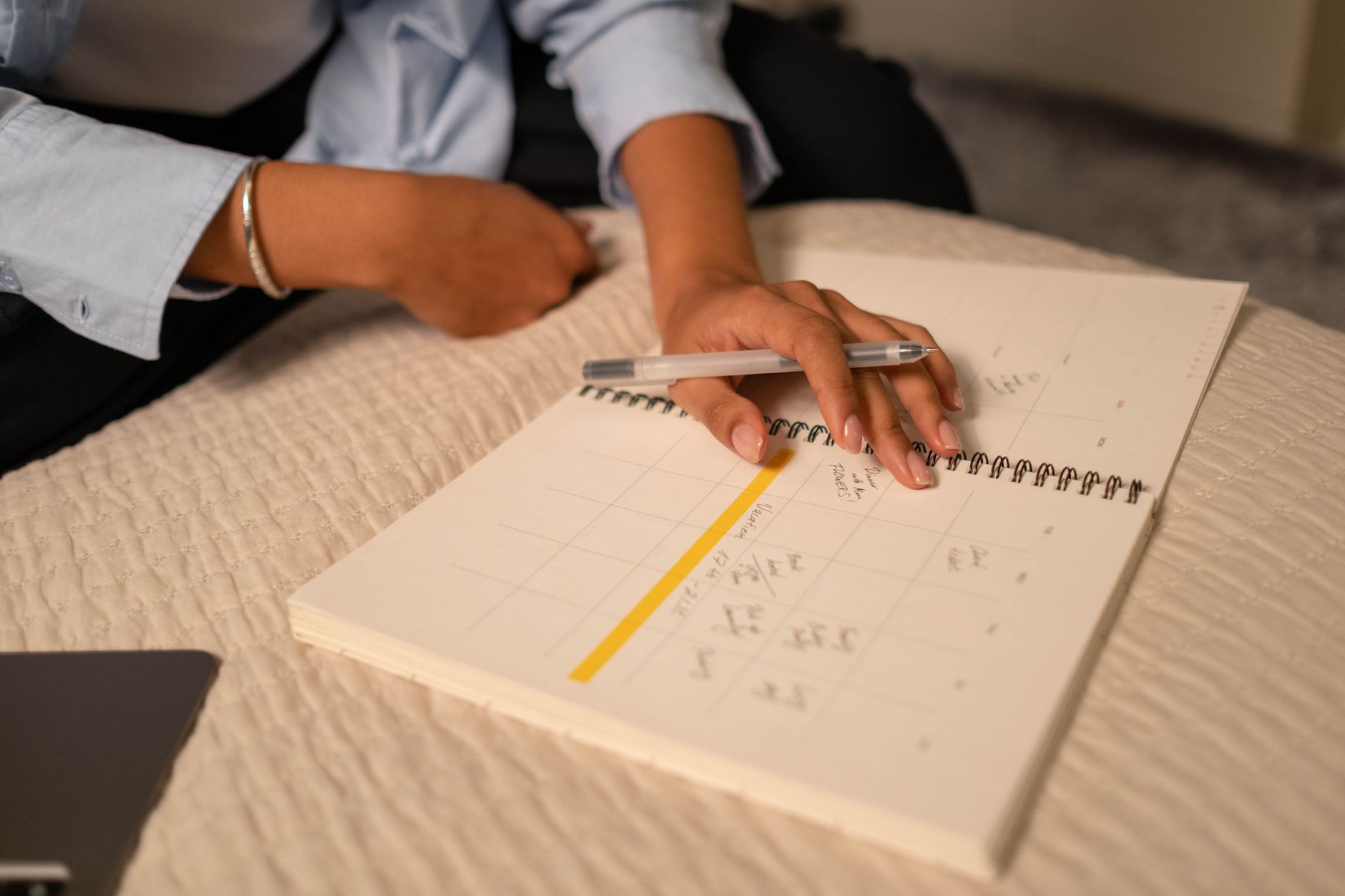 A woman writes on a calendar while sitting on a bed, focusing on her menstrual cycle.