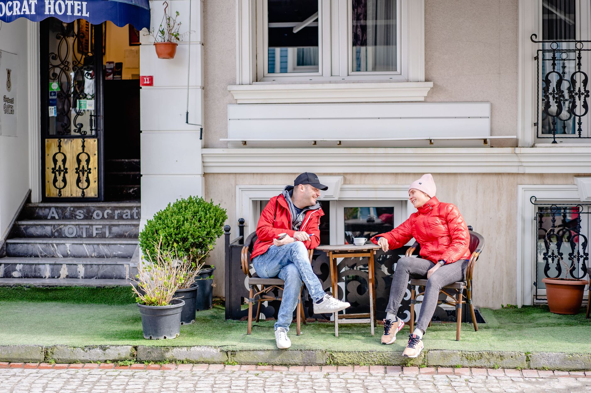 Two friends enjoying conversation outside a hotel in Istanbul, wearing matching red jackets.