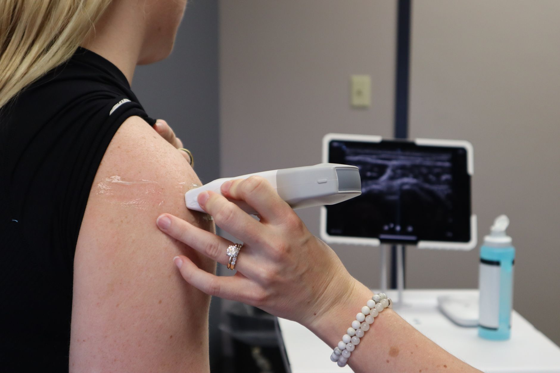 A doctor performing an ultrasound-guided injection on a patient's shoulder while monitoring live imaging.