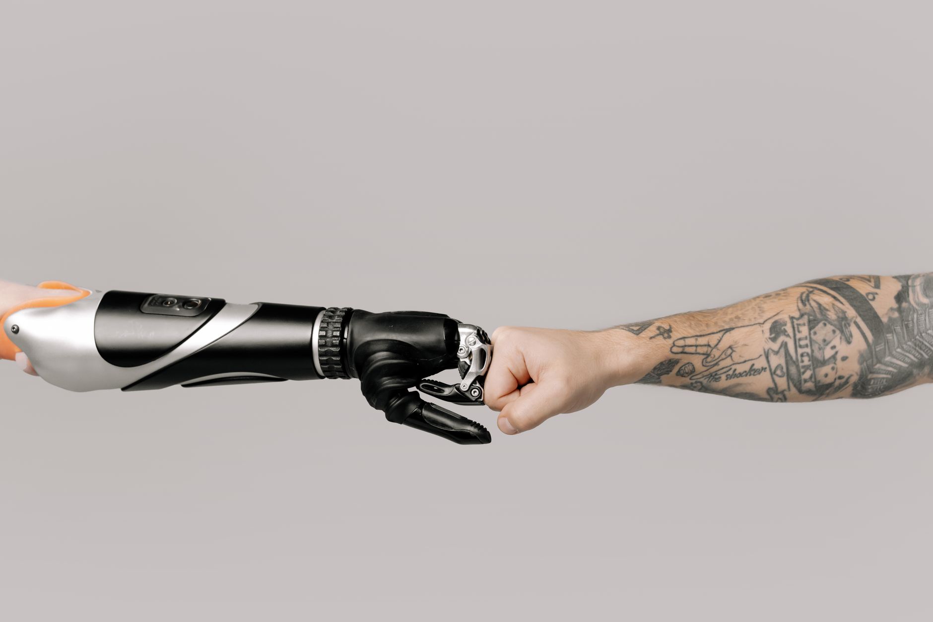 A human hand and a robotic prosthetic arm fist bumping, symbolizing technology and humanity.