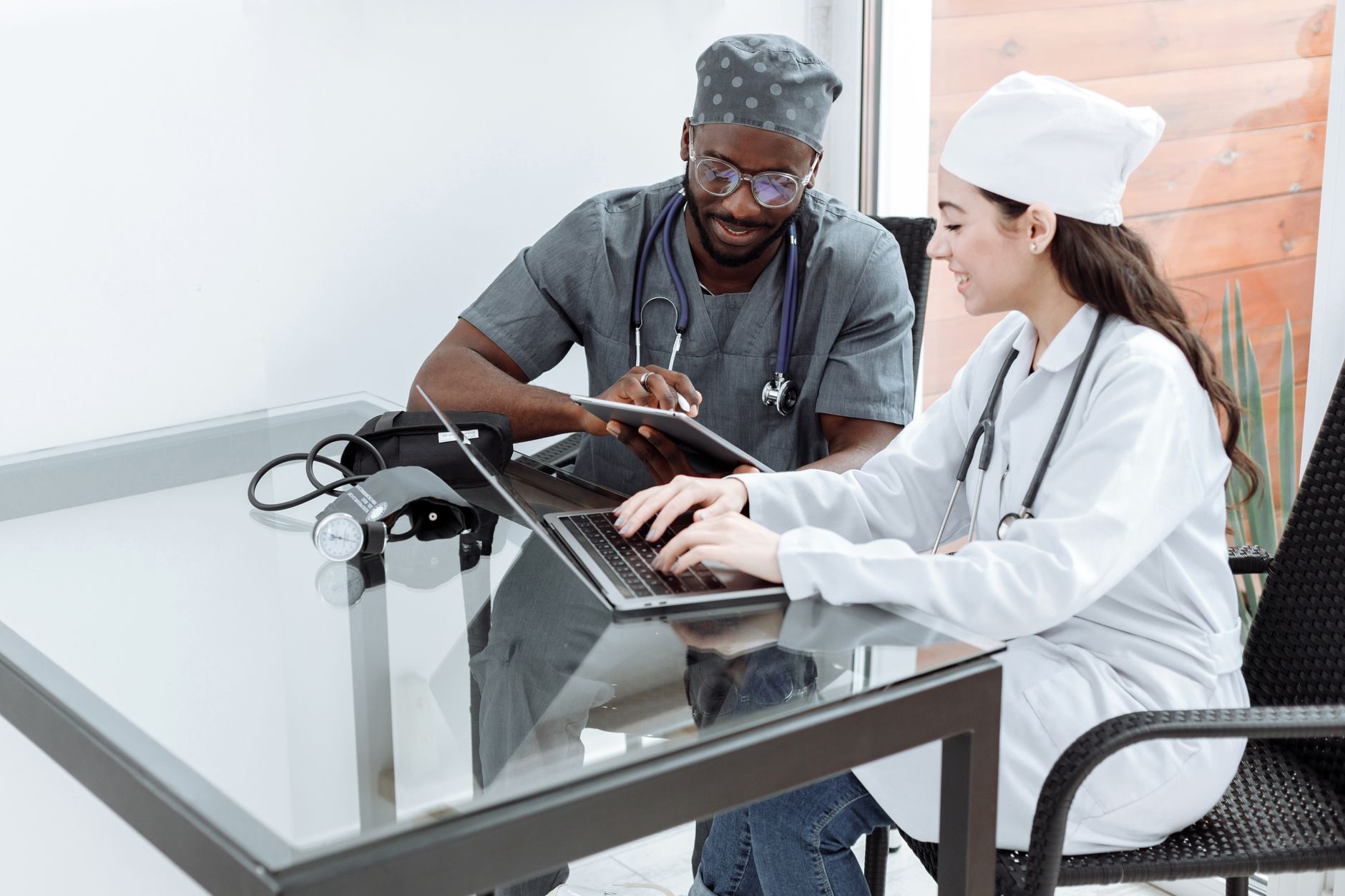 Two doctors discussing pediatric case, one on tablet and one on laptop at a table.