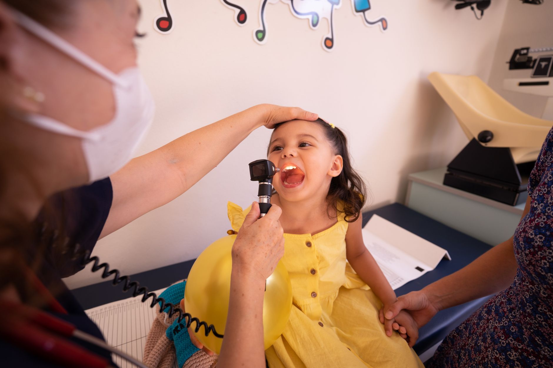 A young girl laughing as a doctor examines her throat in a hospital.