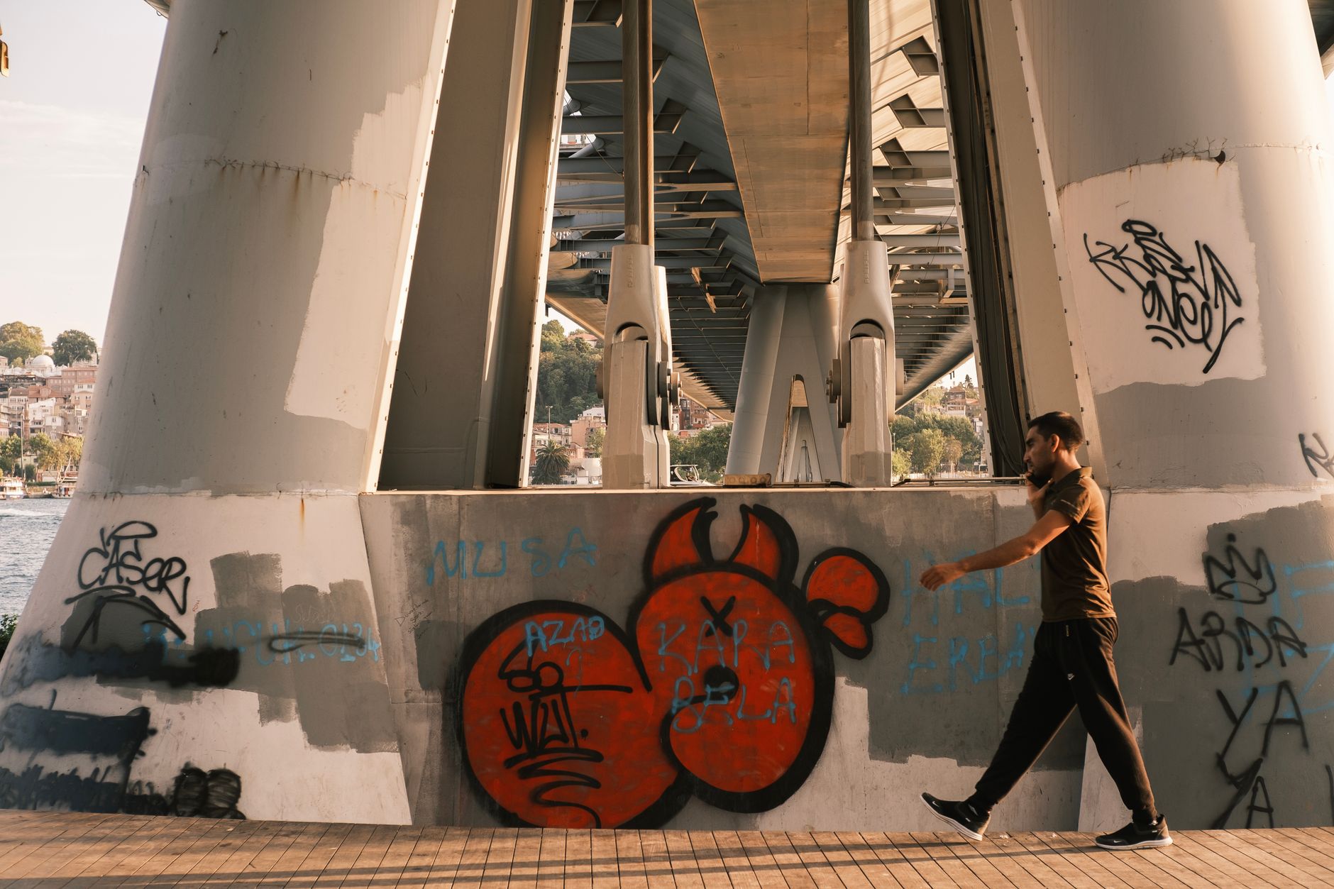 A man walks near graffiti-covered pillars under a bridge by the Bosphorus.