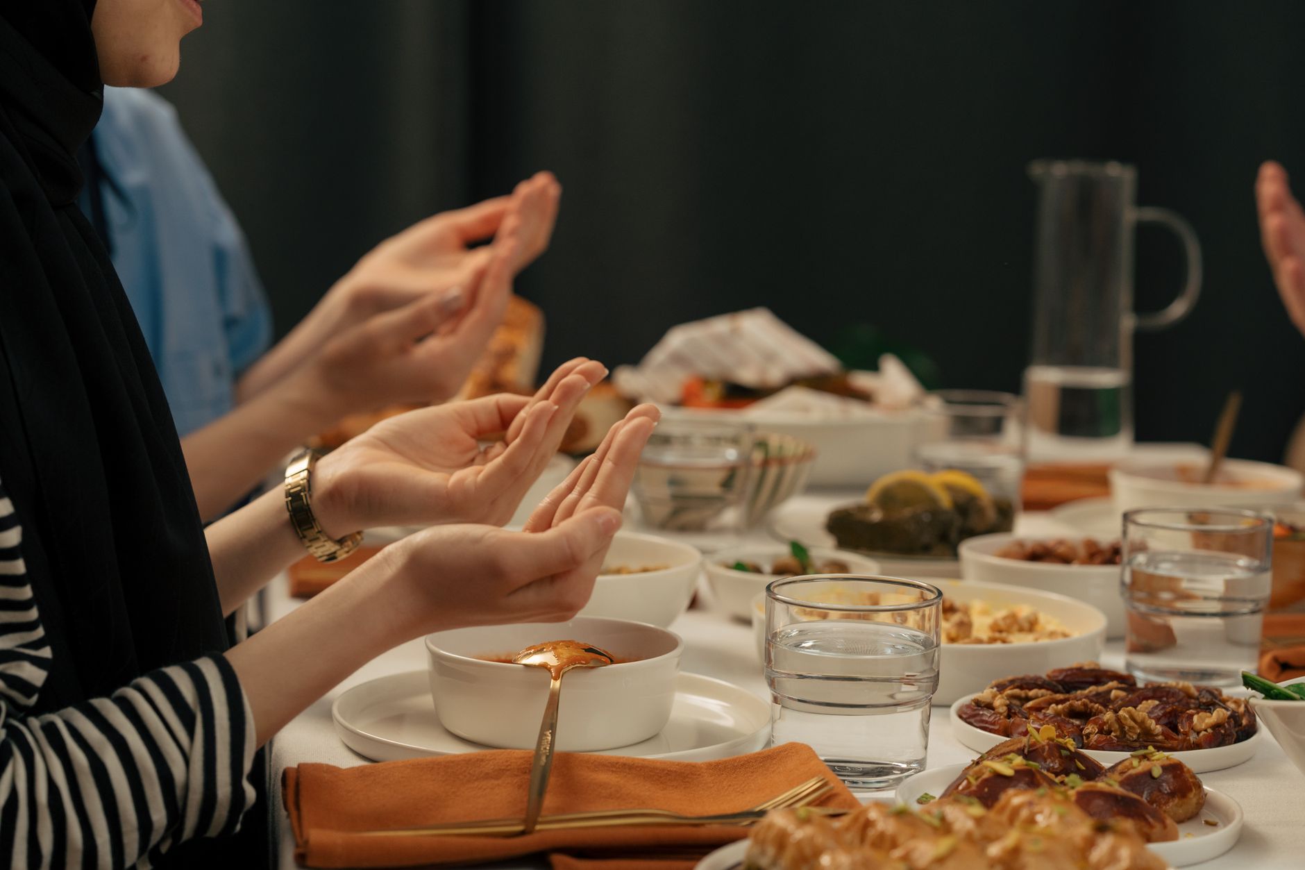 Communal iftar dinner scene showcasing hands in prayer, diverse dishes, and an ambiance of Turkish hospitality.