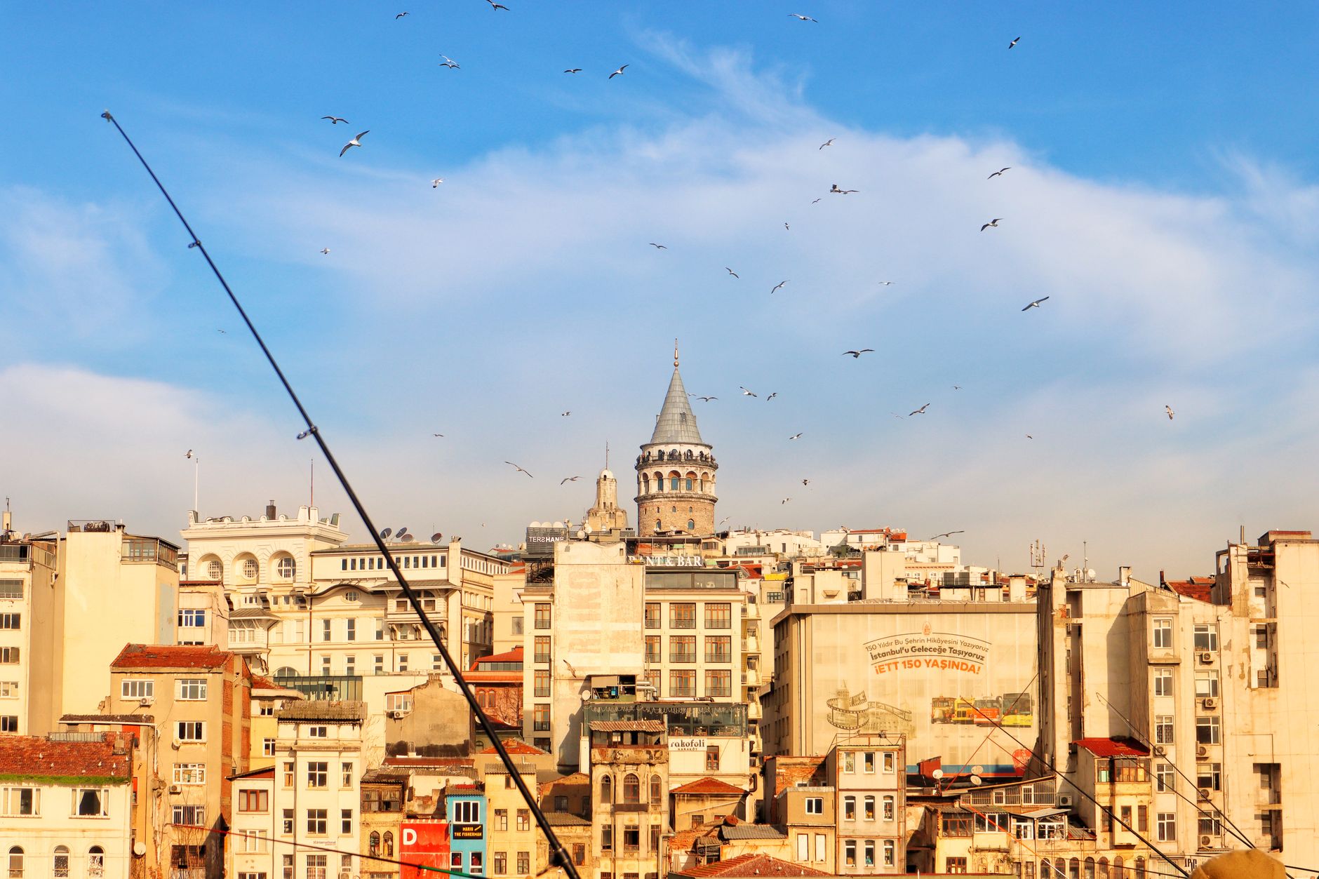 A scenic view of Istanbul's Galata Tower surrounded by buildings and birds in a clear blue sky.