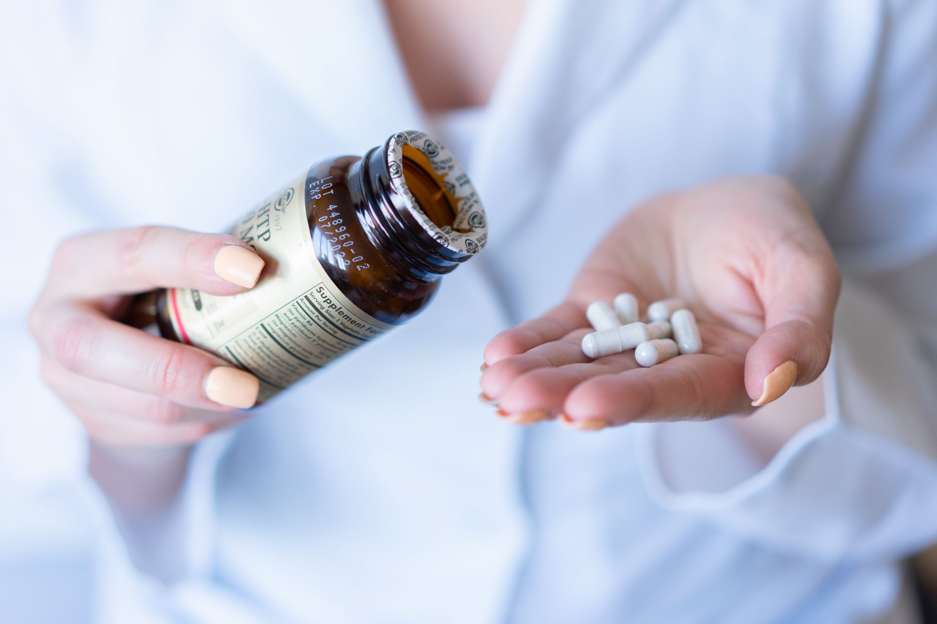 A hand holding a pill bottle and several capsules, representing a micronutrient schedule.