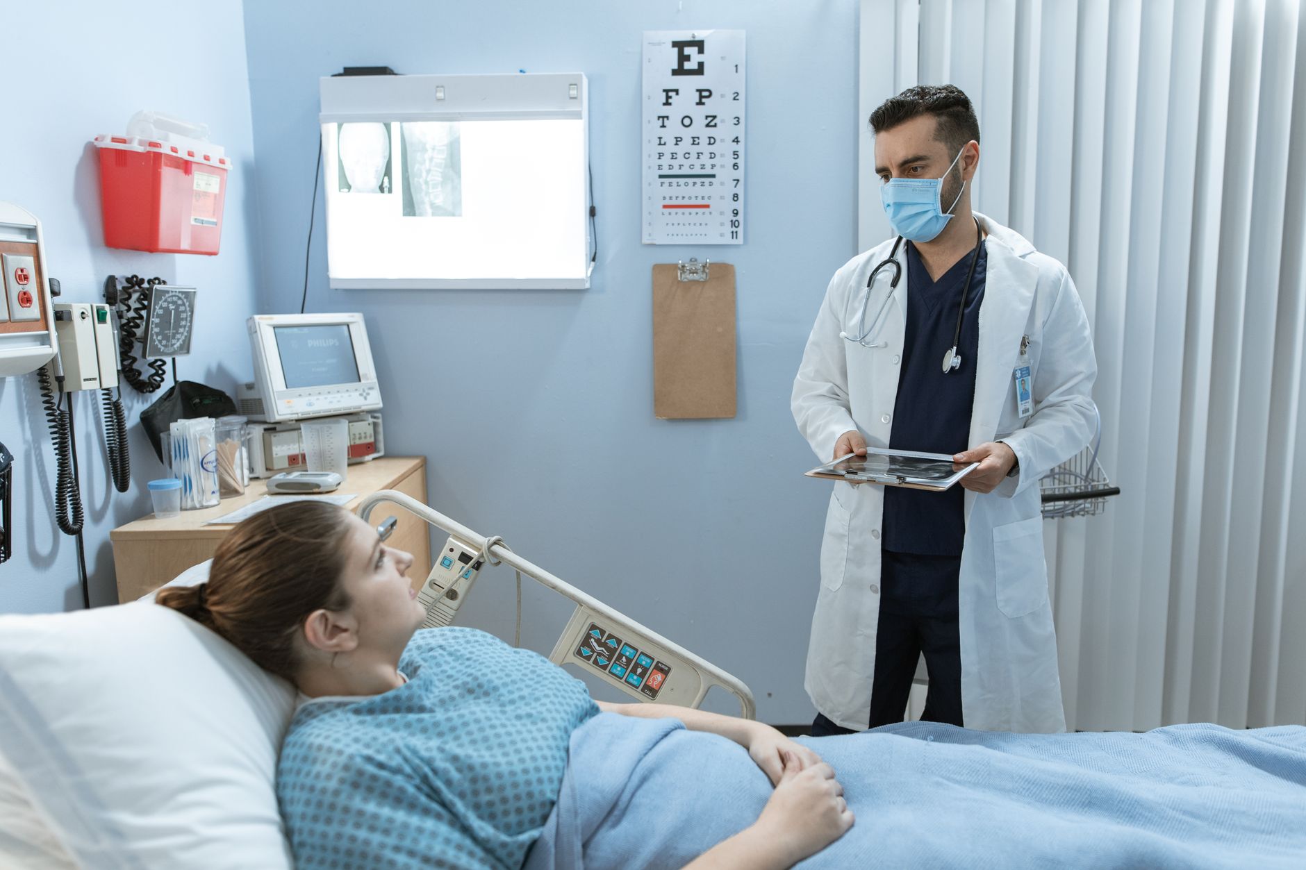 A doctor in a white coat explains treatment to a patient in a hospital bed.