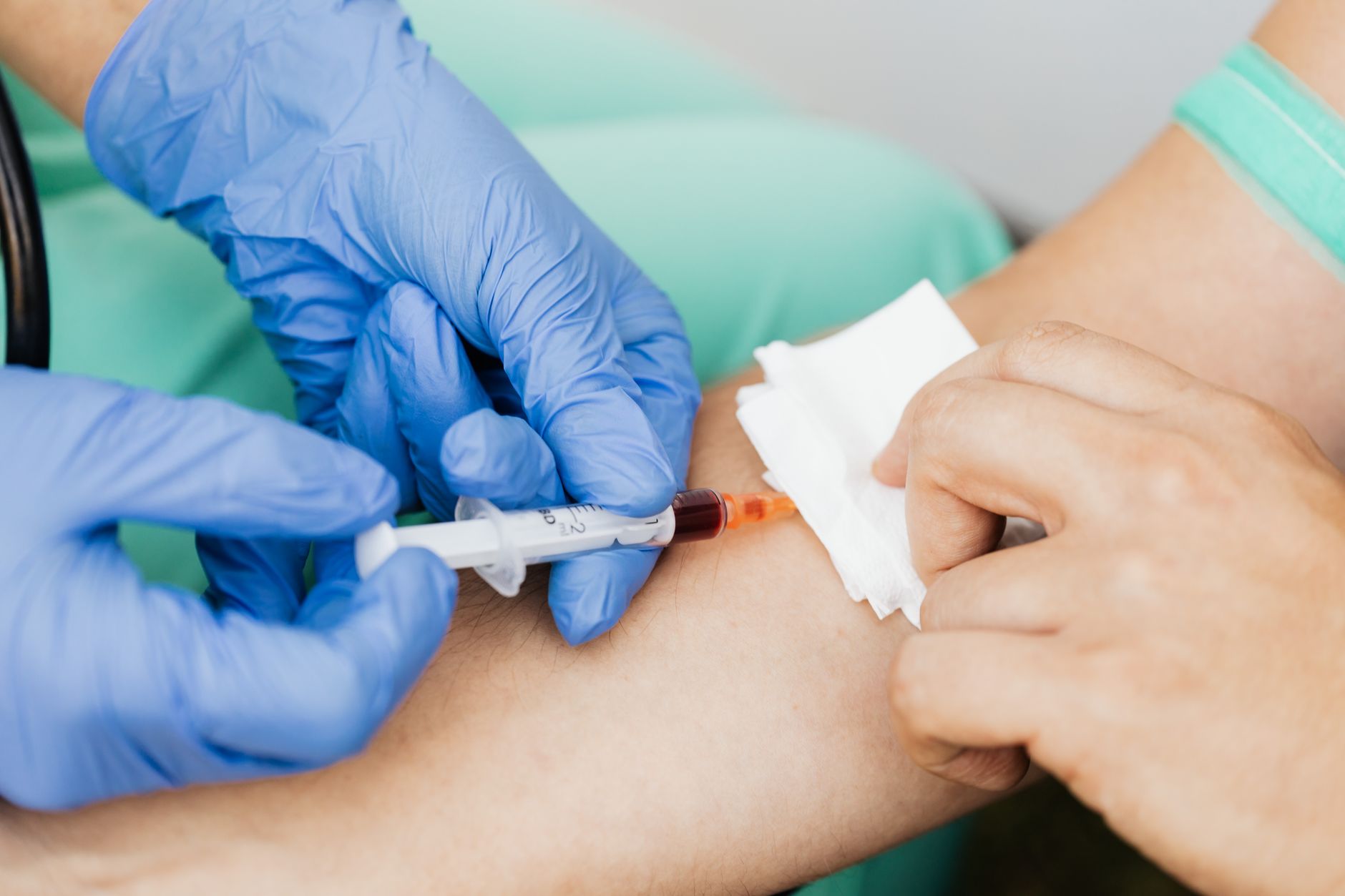 A nurse in blue gloves draws blood from a patient's arm in a clinic.