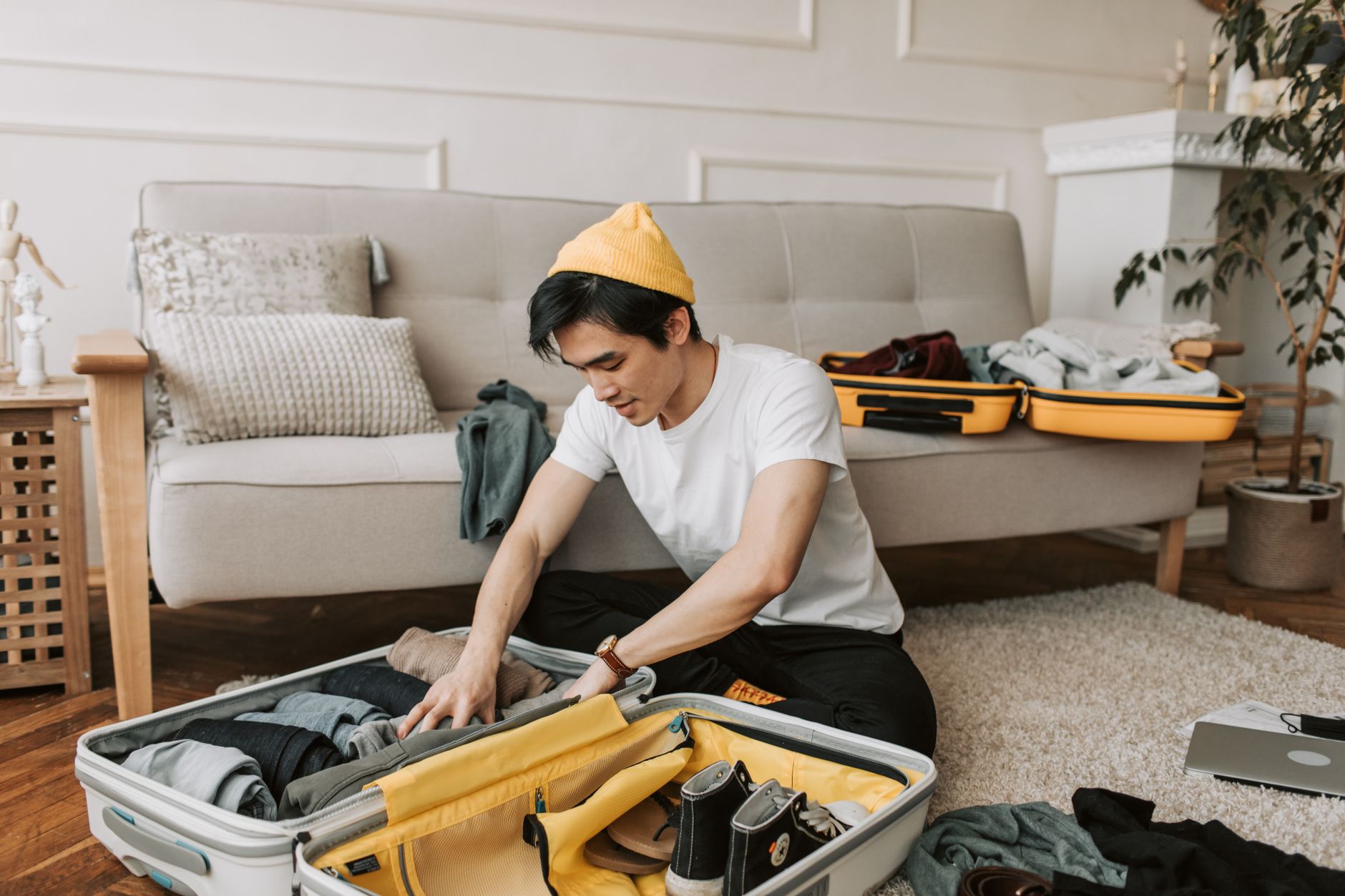 A young man packing clothes and shoes in a suitcase at home.