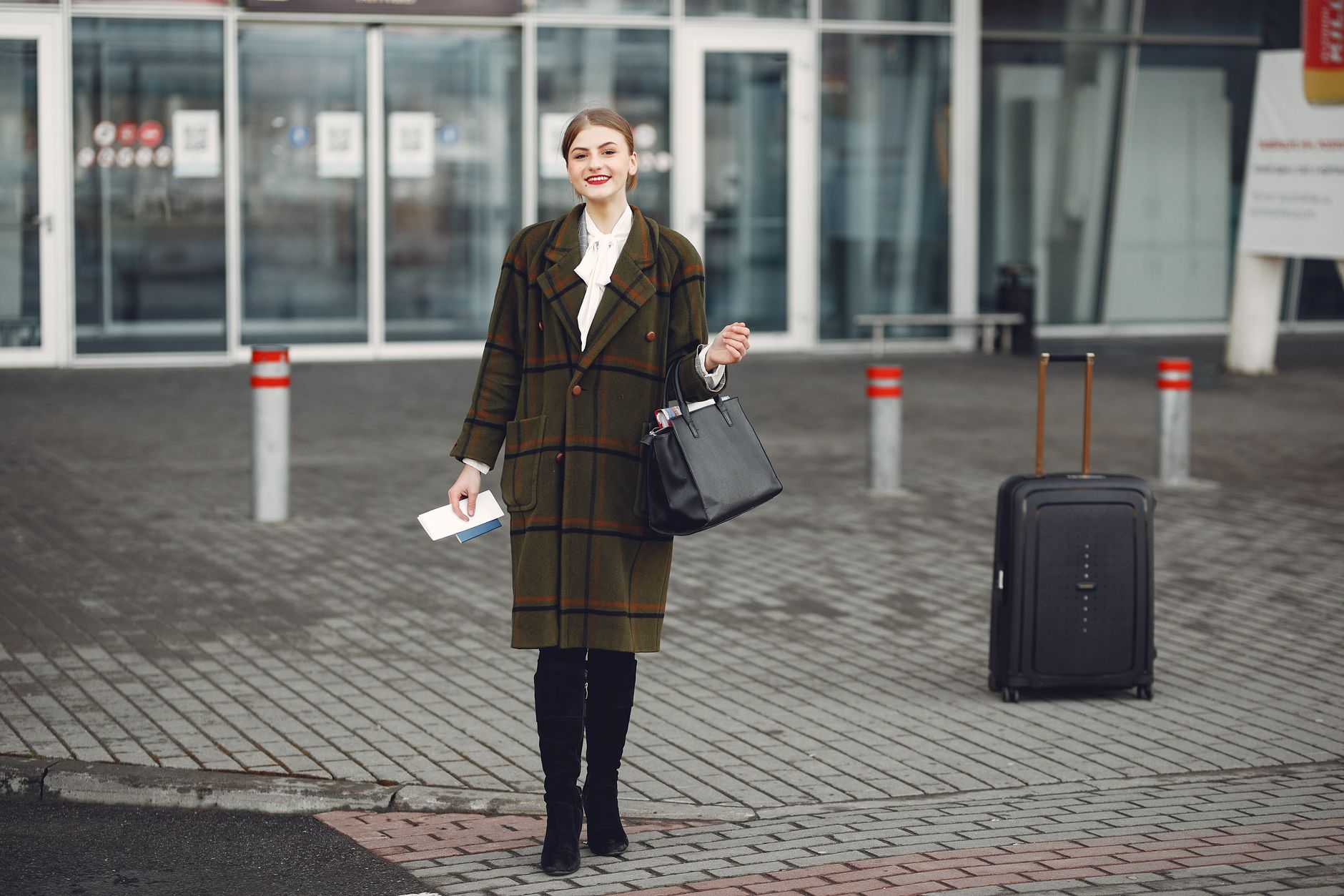 A woman in a green coat holding medical documents at the airport, ready to depart for Türkiye.