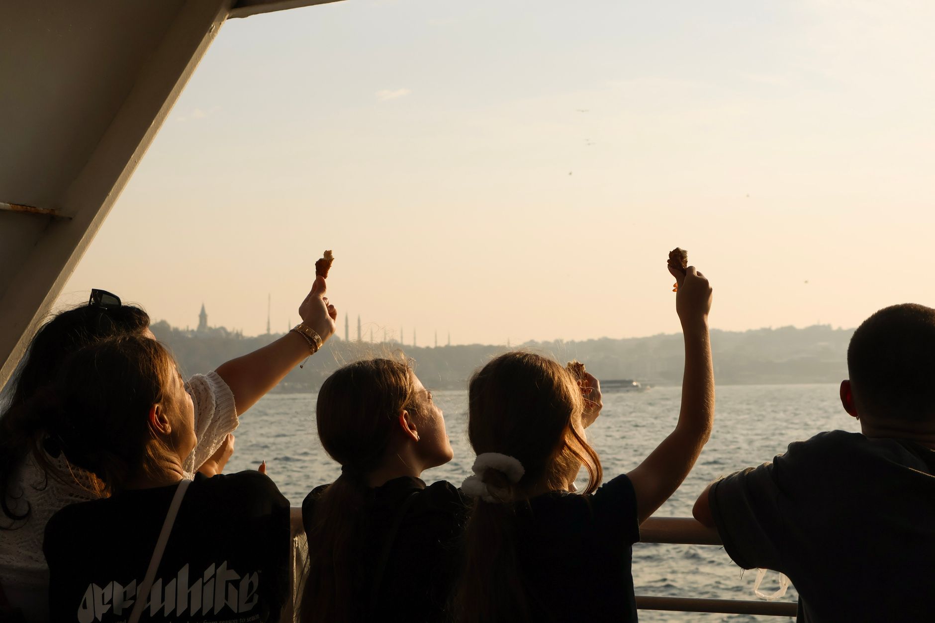 A family on a boat in Istanbul raises snacks while enjoying the Bosphorus view.