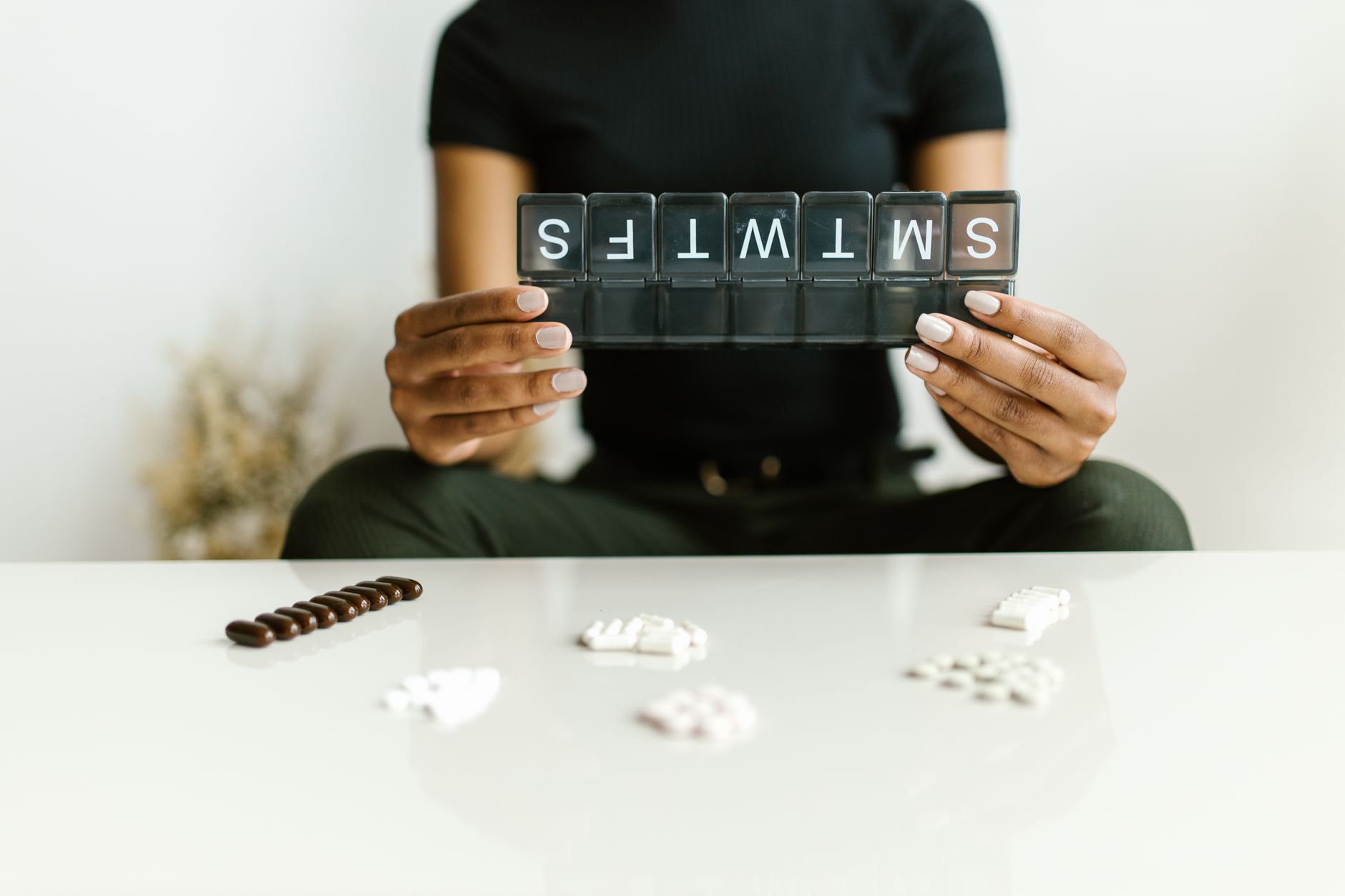 A person holding a pill organizer labeled 'SMWTS', with various medications arranged on a table.