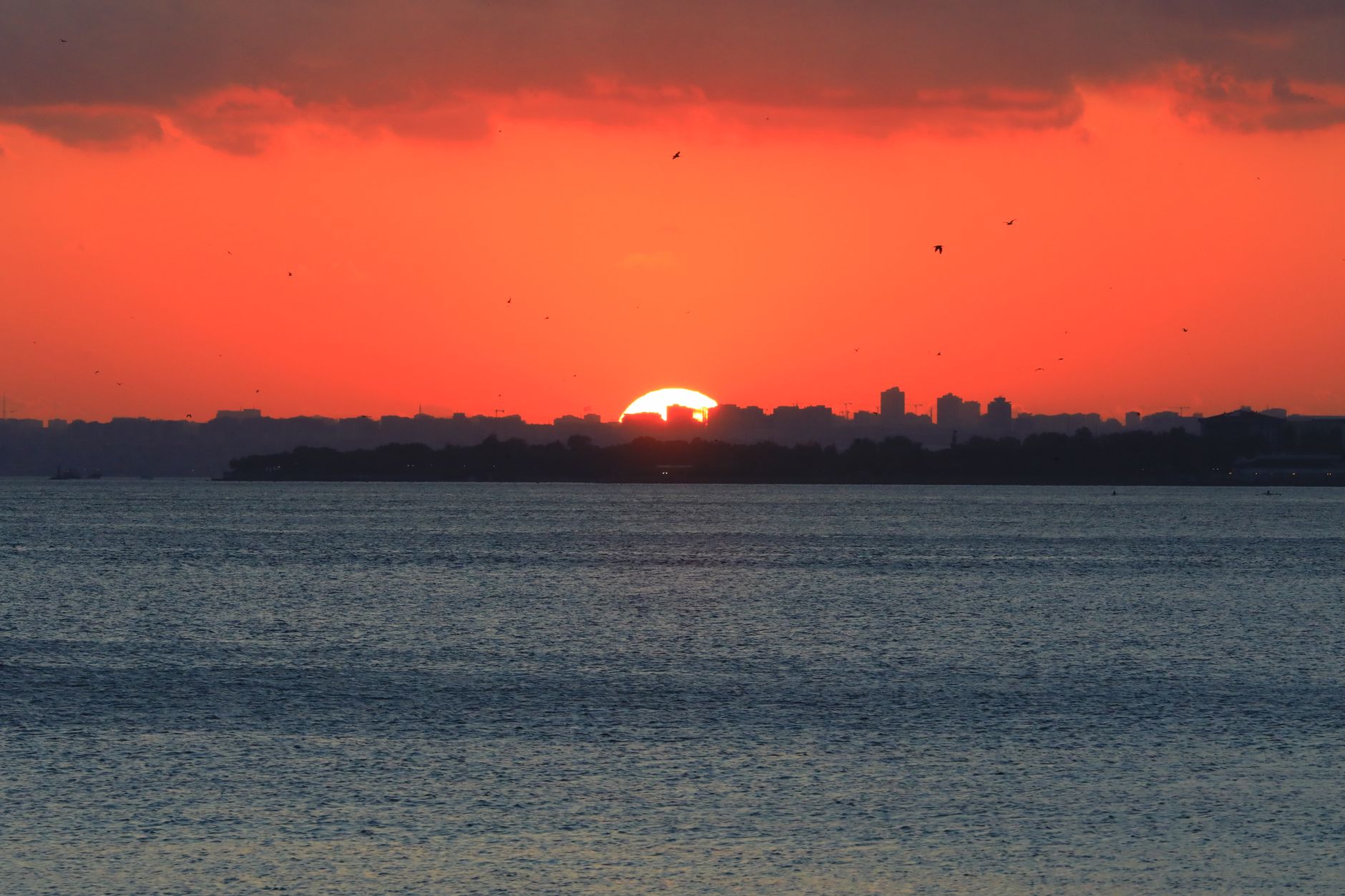 A breathtaking sunset casts an orange glow over Istanbul's skyline and the tranquil water below.