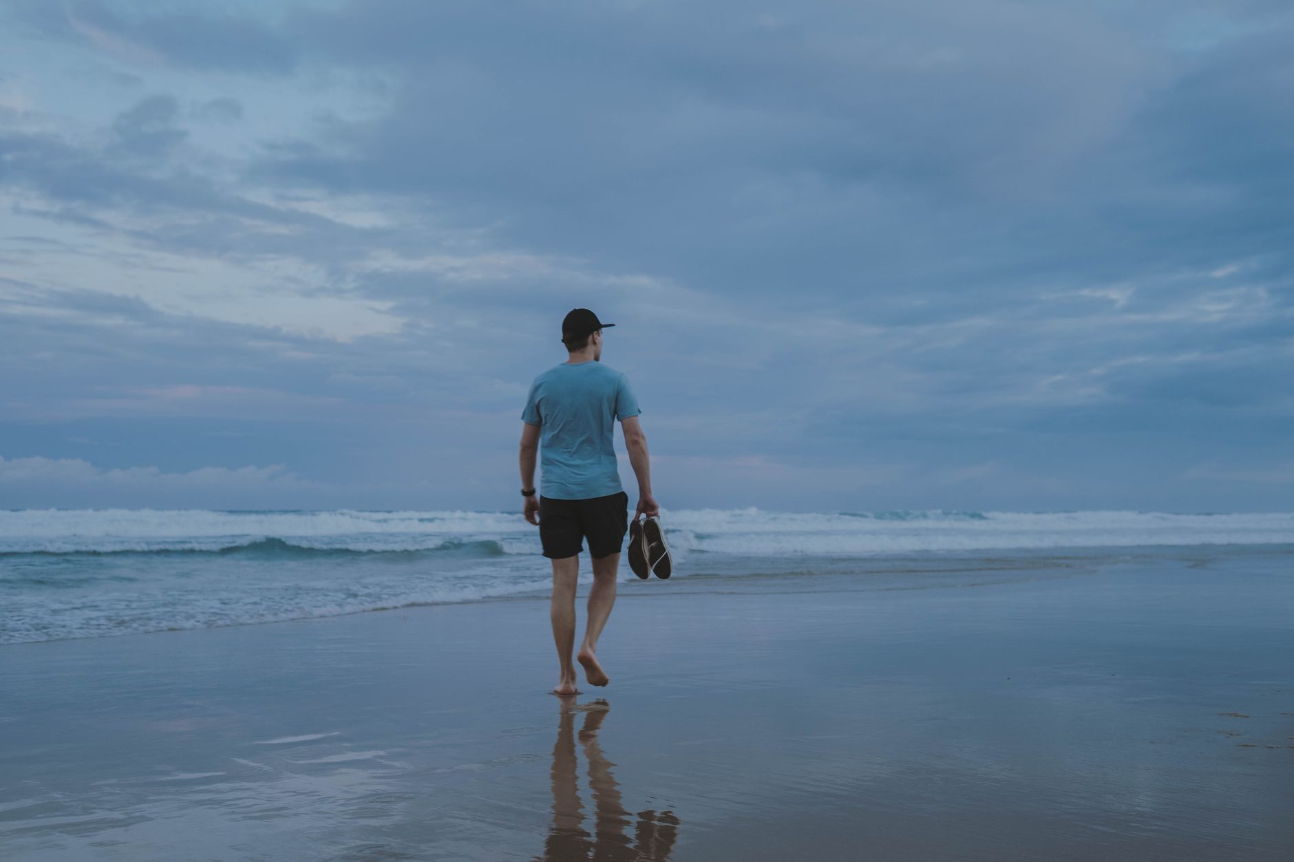 A person walking barefoot along the beach in Antalya, holding shoes, reflecting on recovery.