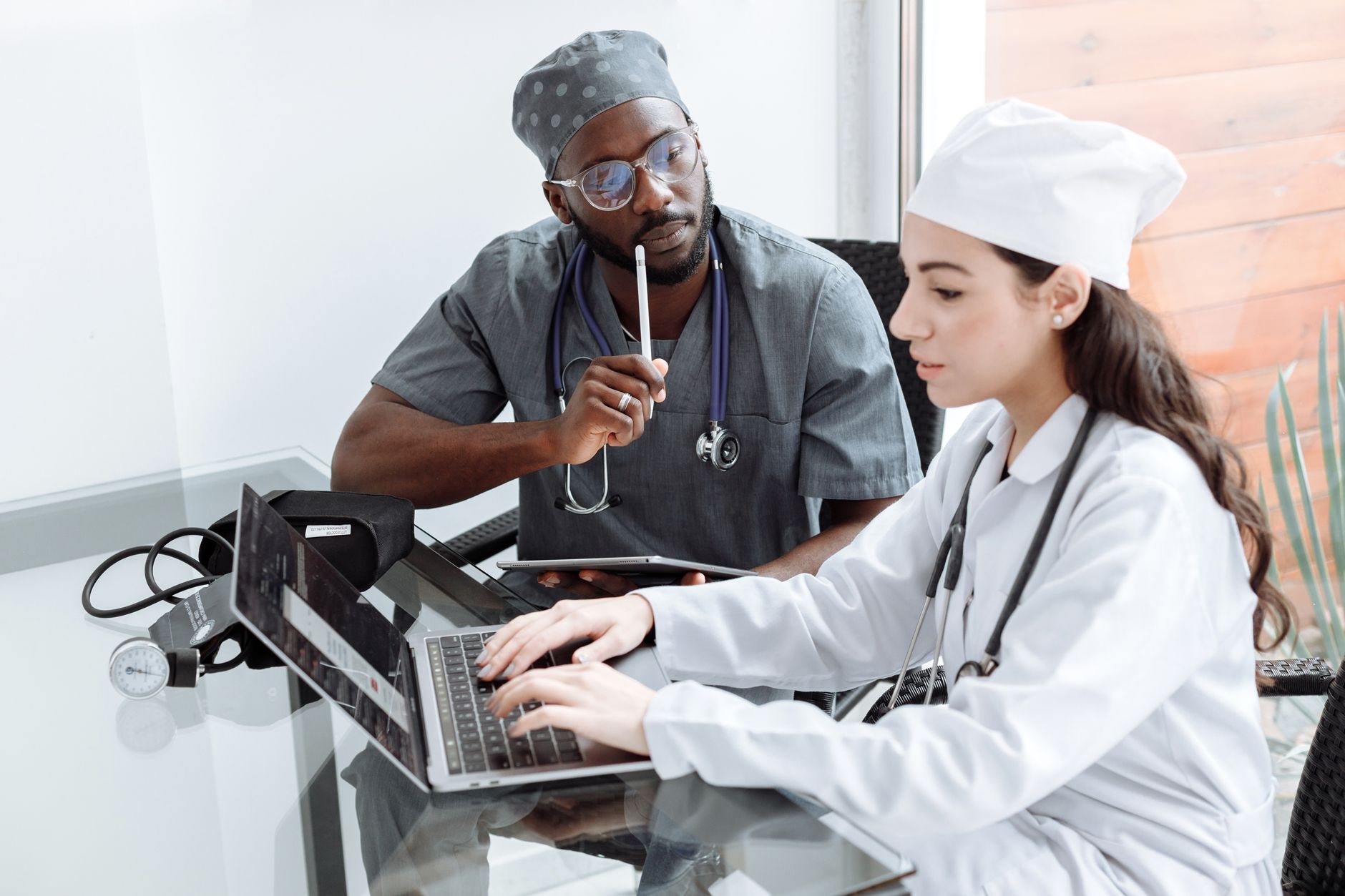 Two medical professionals discussing treatment plans over a laptop at a glass table.