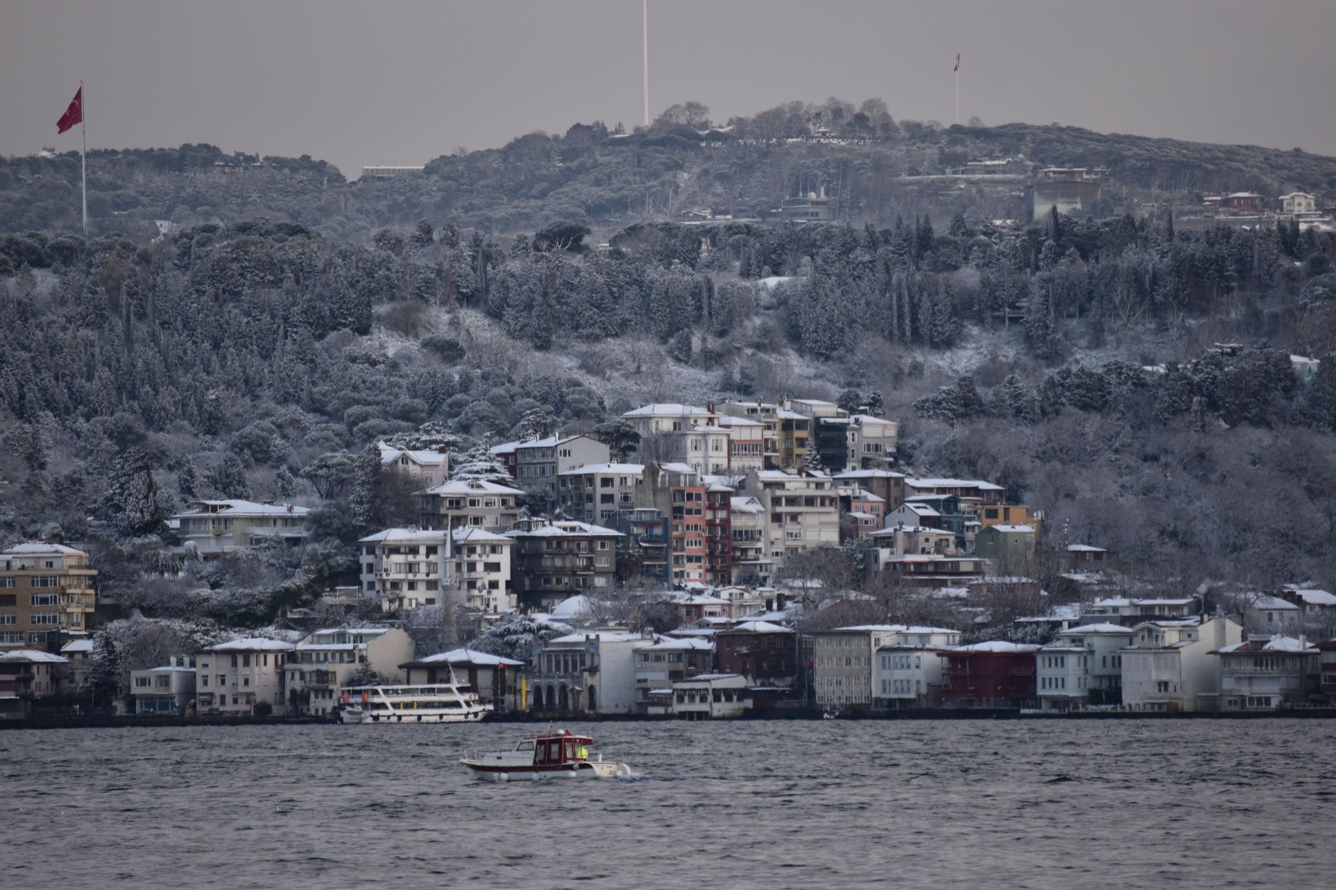 A picturesque winter scene in Istanbul showing snow-covered buildings and a boat on the water.