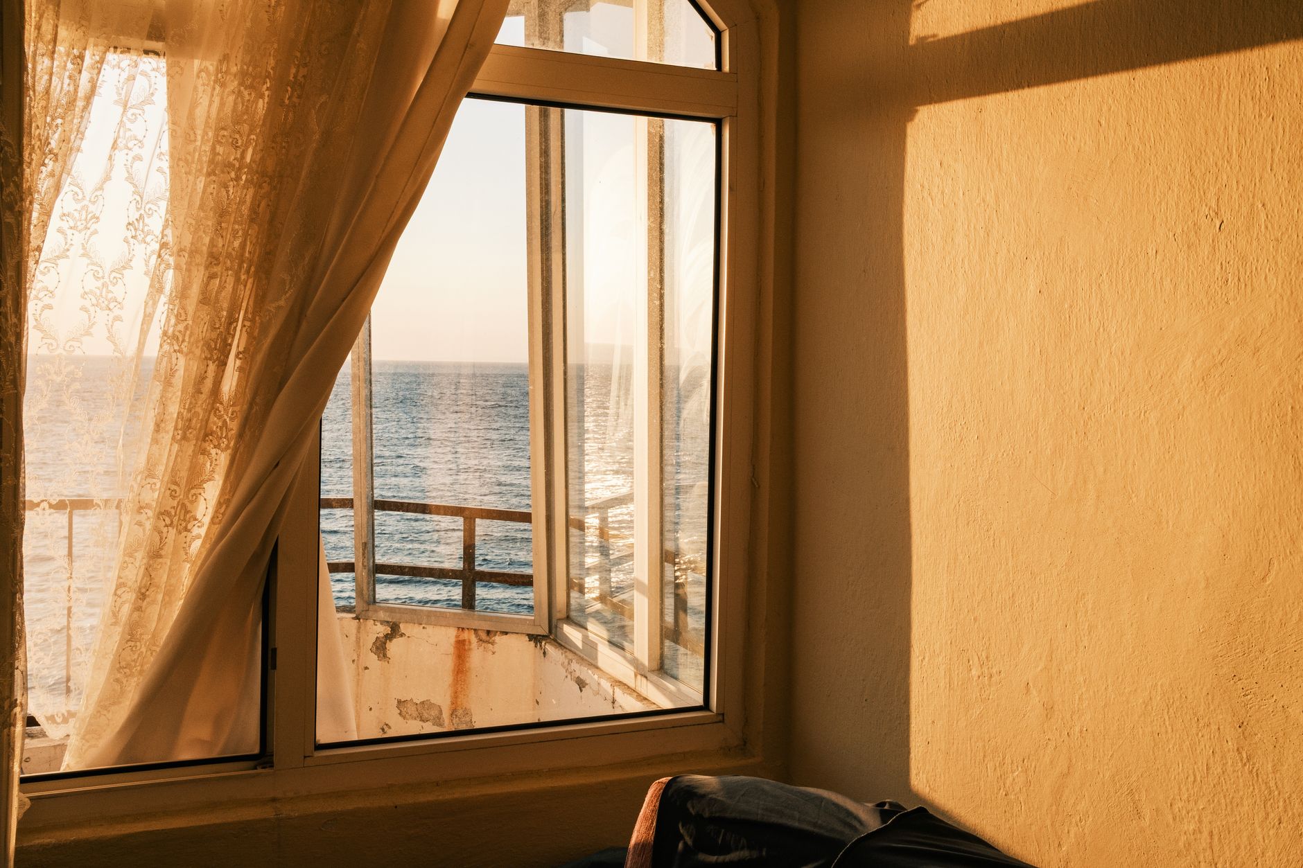 Interior of a peaceful room with a sea view, soft light through lace curtains.