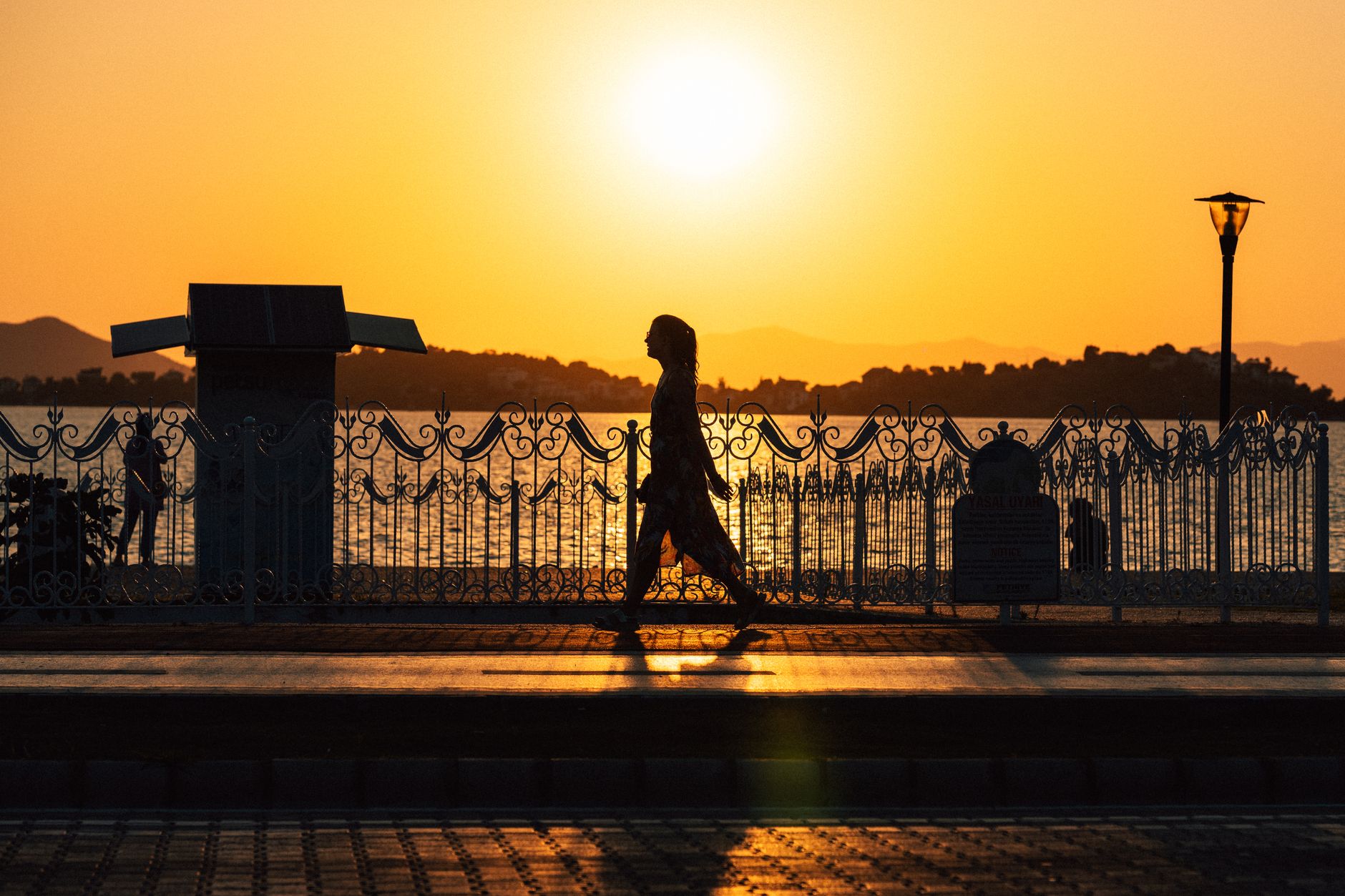 Silhouette of a woman walking on Fethiye promenade at sunset, with ocean view.