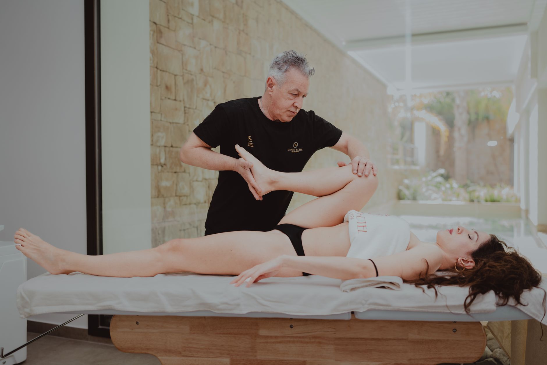 A physiotherapist assists a patient with leg mobilization on a massage table.