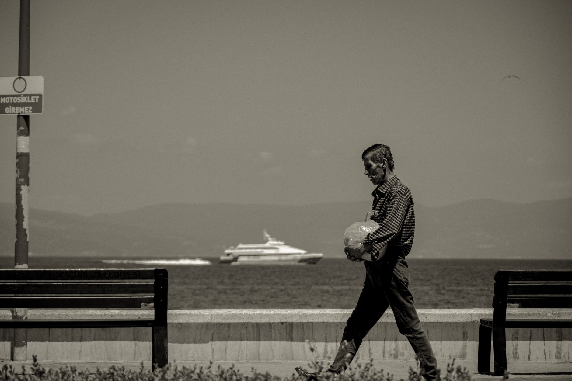 A man walking along the waterfront in Bursa, holding a bag, with a yacht in the background.