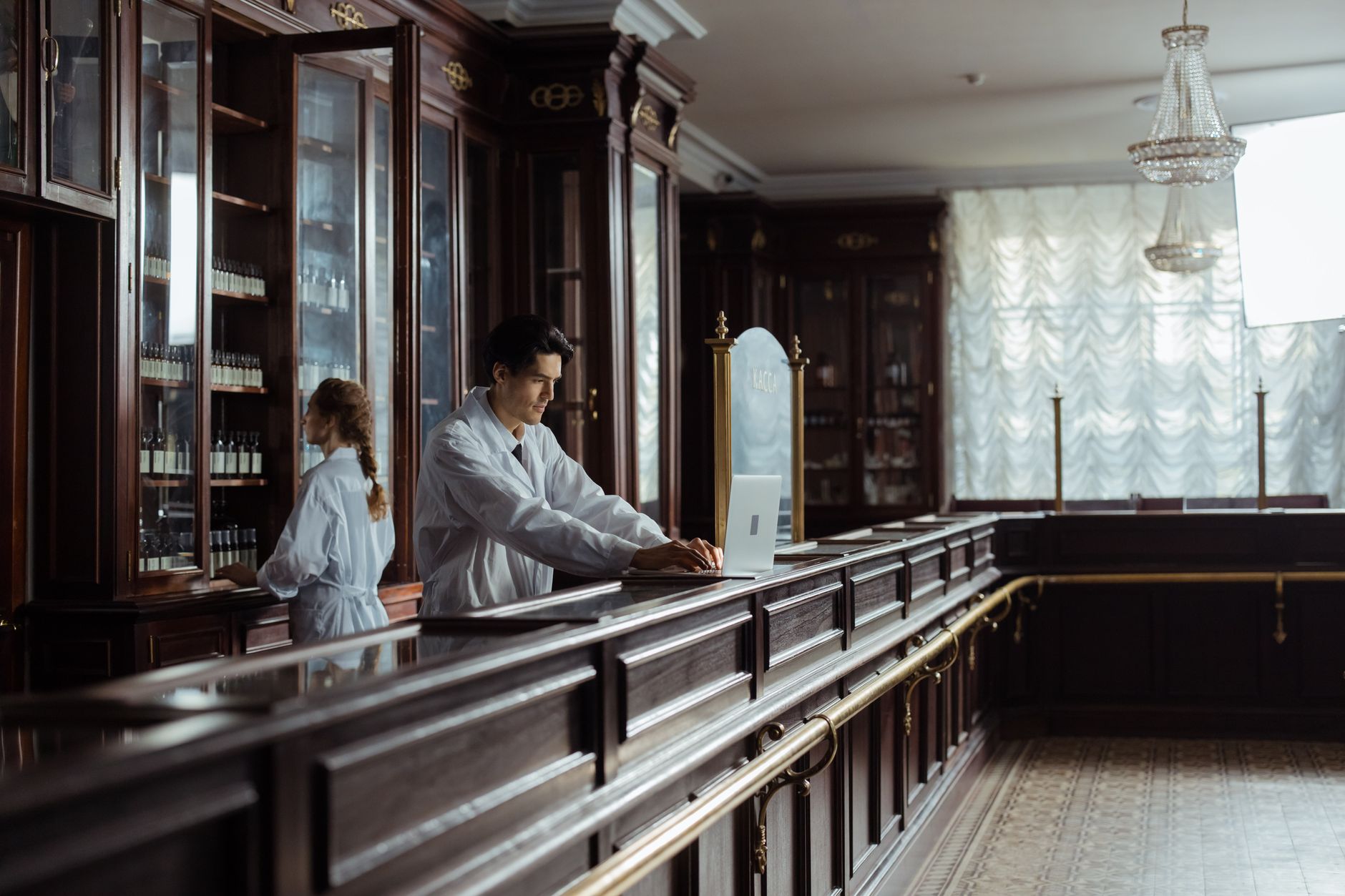 A pharmacist in a white coat assisting a patient in a vintage pharmacy setting.