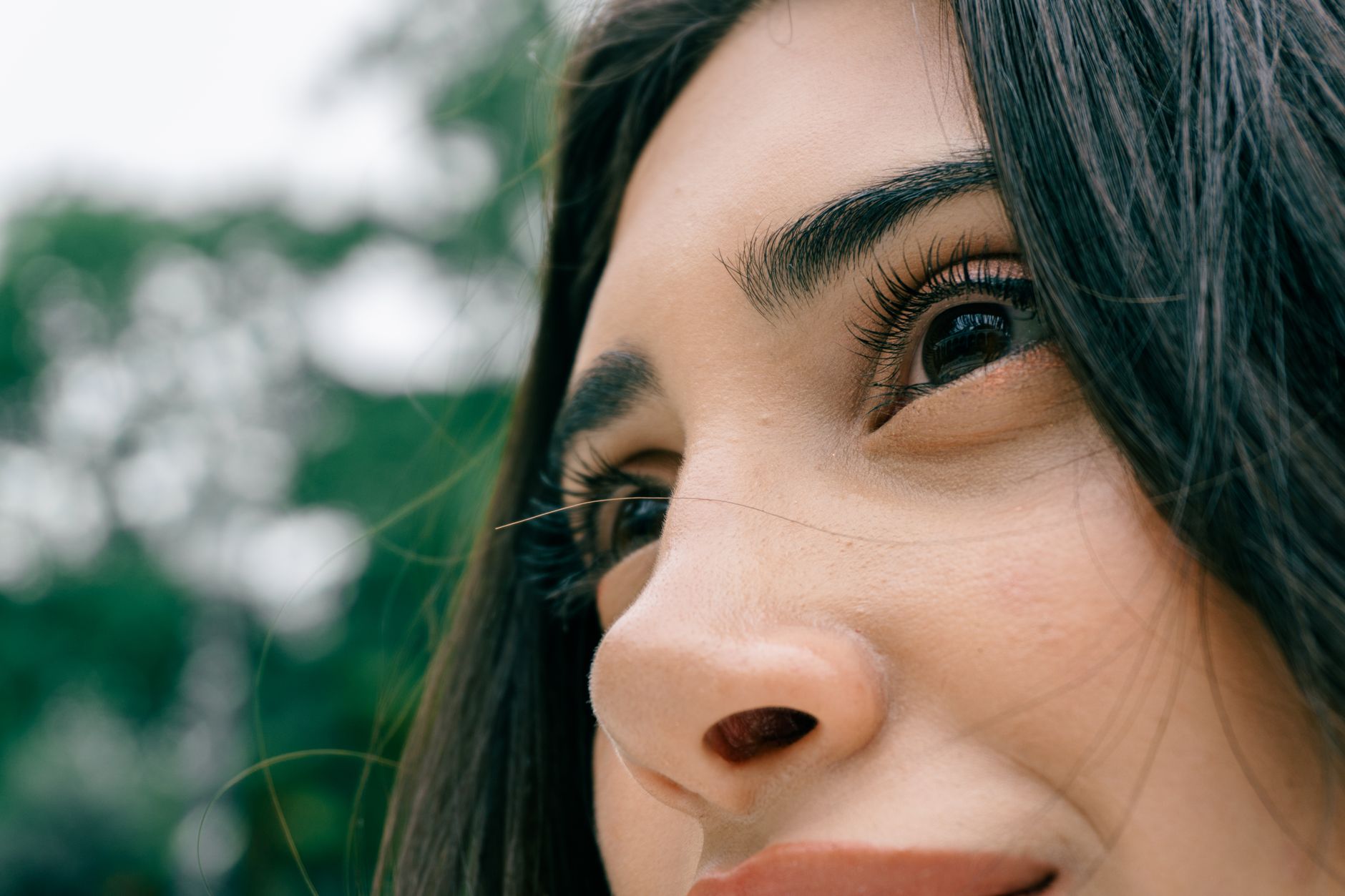 Close-up of a woman's face, highlighting her eyes and skin in a natural outdoor setting.