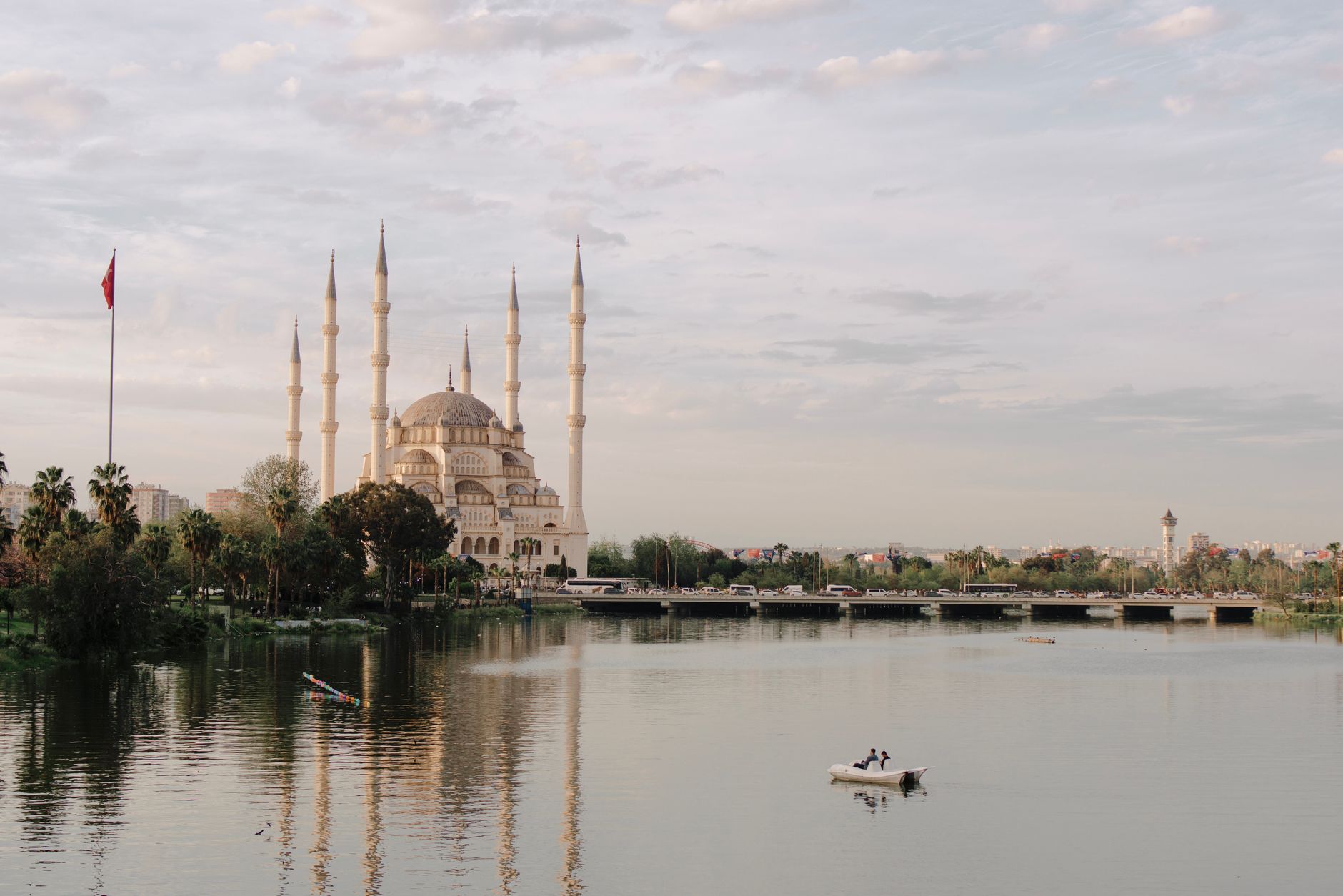 Sabancı Central Mosque by the river in Adana, with people boating nearby.