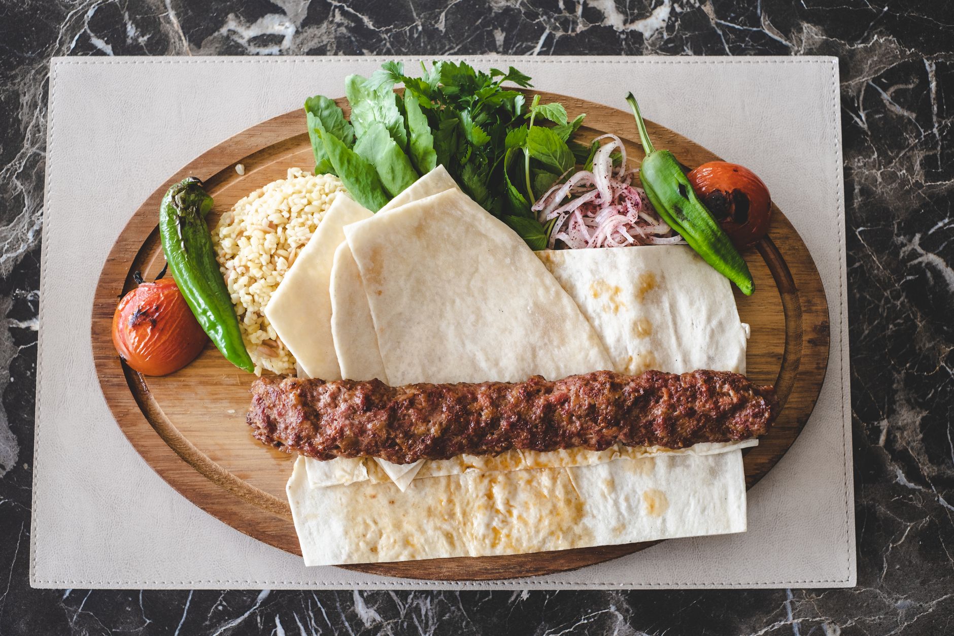A vibrant Adana kebab platter featuring grilled meat, fresh greens, and sides.