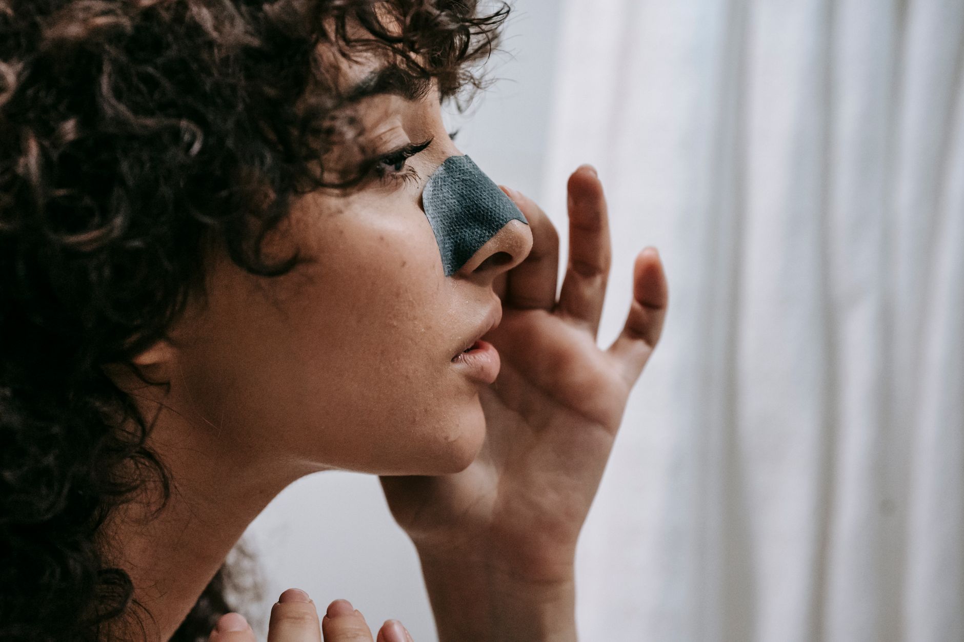 Close-up of a woman applying a nose strip, showcasing her satisfaction.