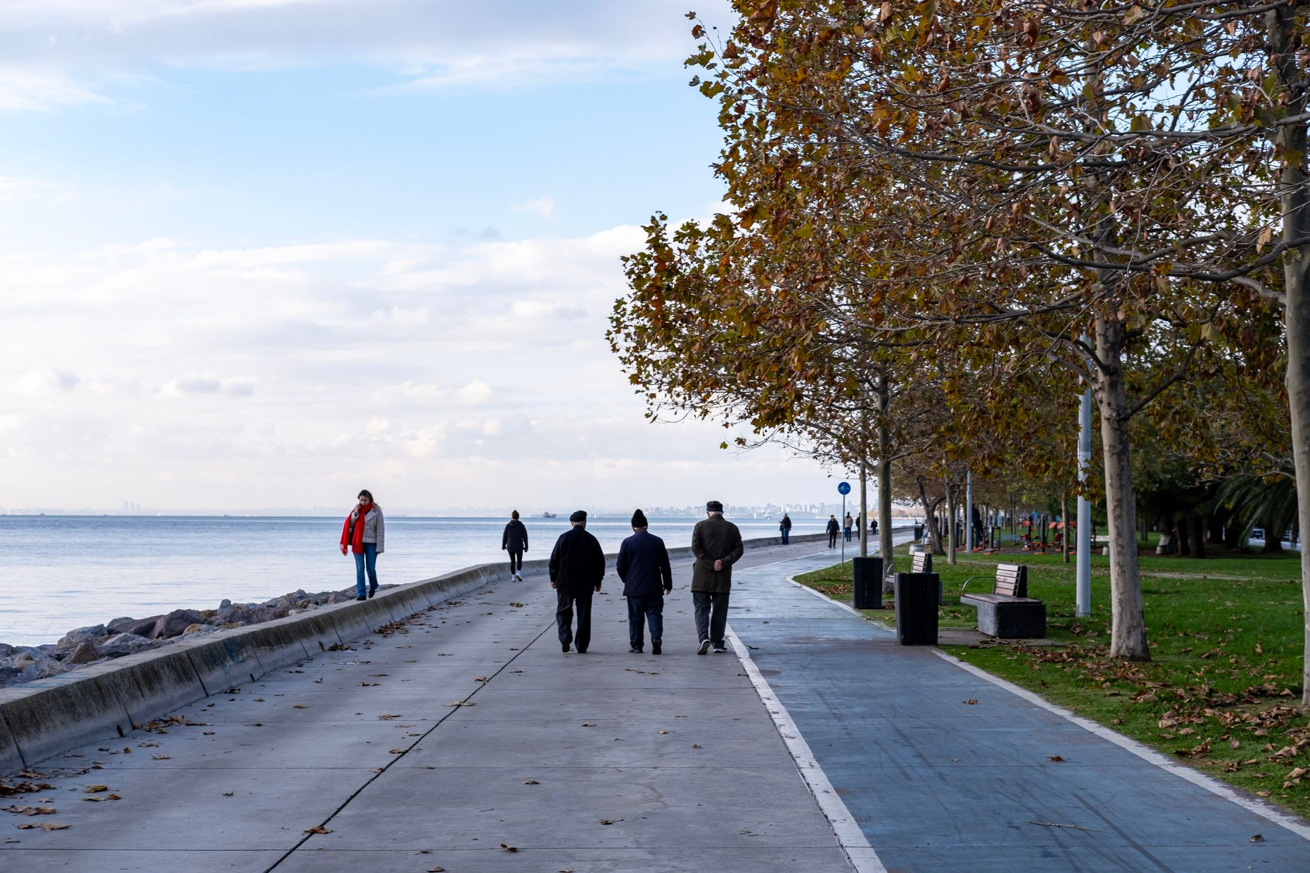 People walking along a peaceful waterfront path in a park by the sea.