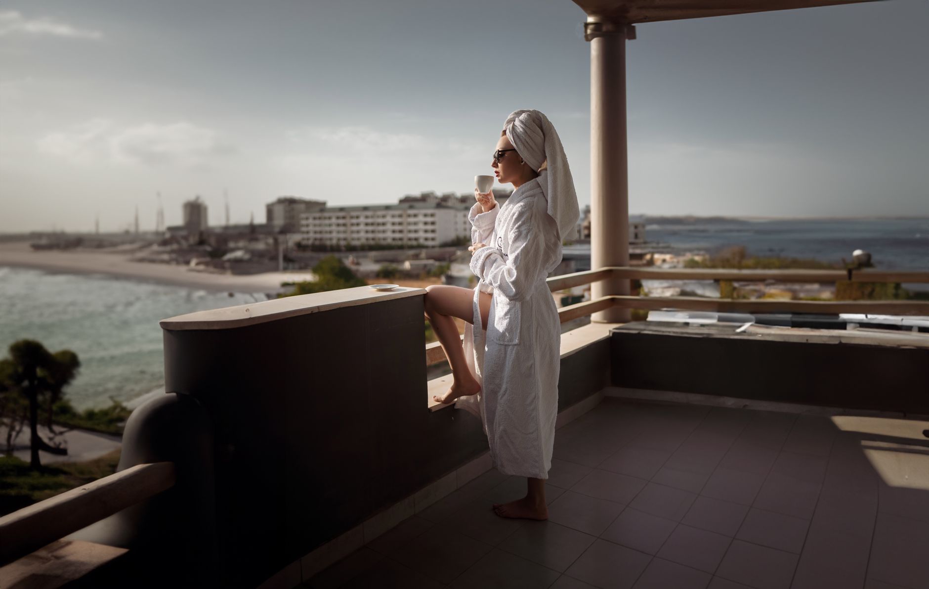 Woman in bathrobe enjoying a serene moment on balcony with Aegean Sea view.