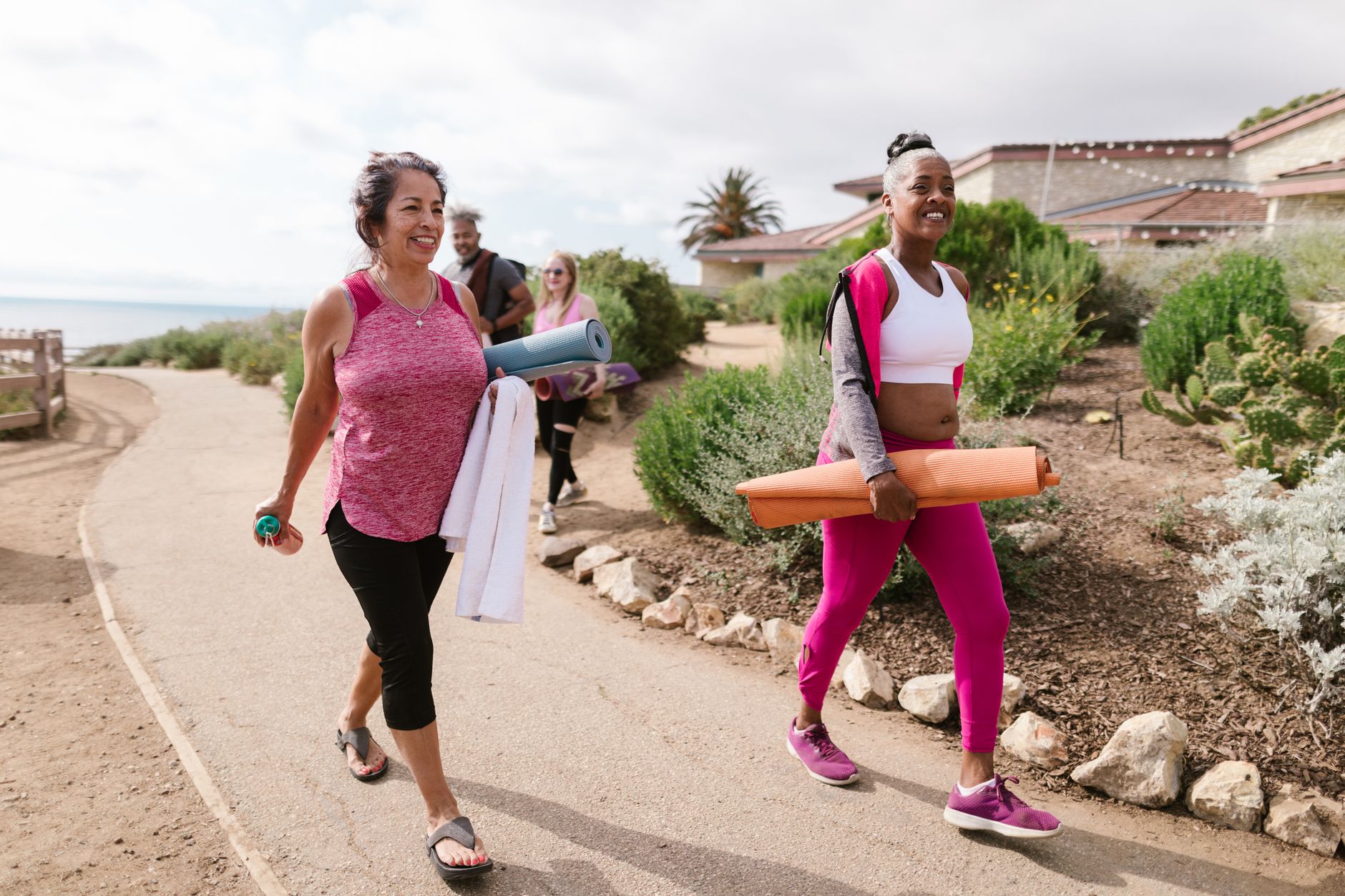 Group of women walking outdoors with yoga mats in a coastal area.