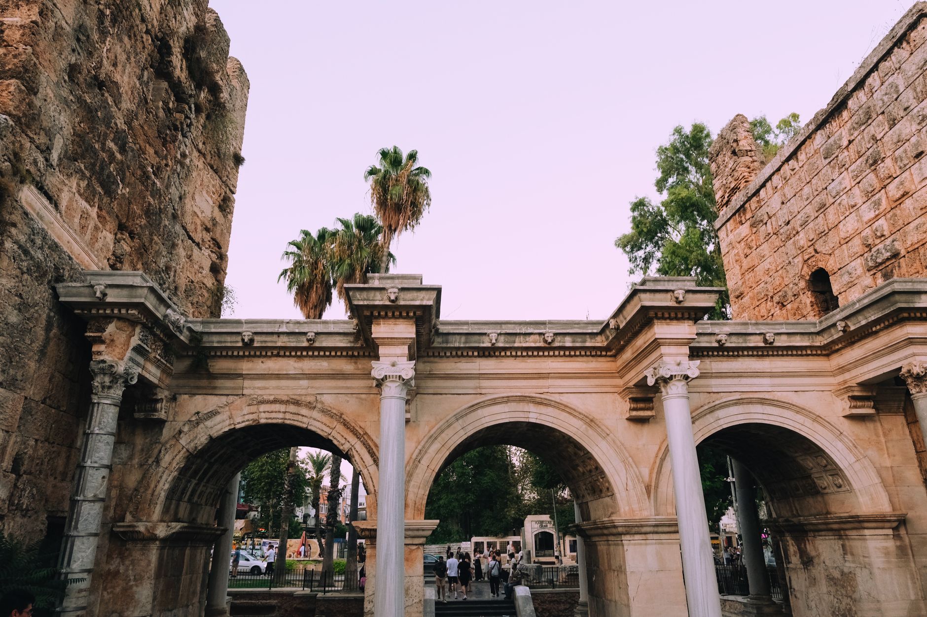 View of Hadrian's Gate in Antalya's Old Town, surrounded by palm trees and visitors.
