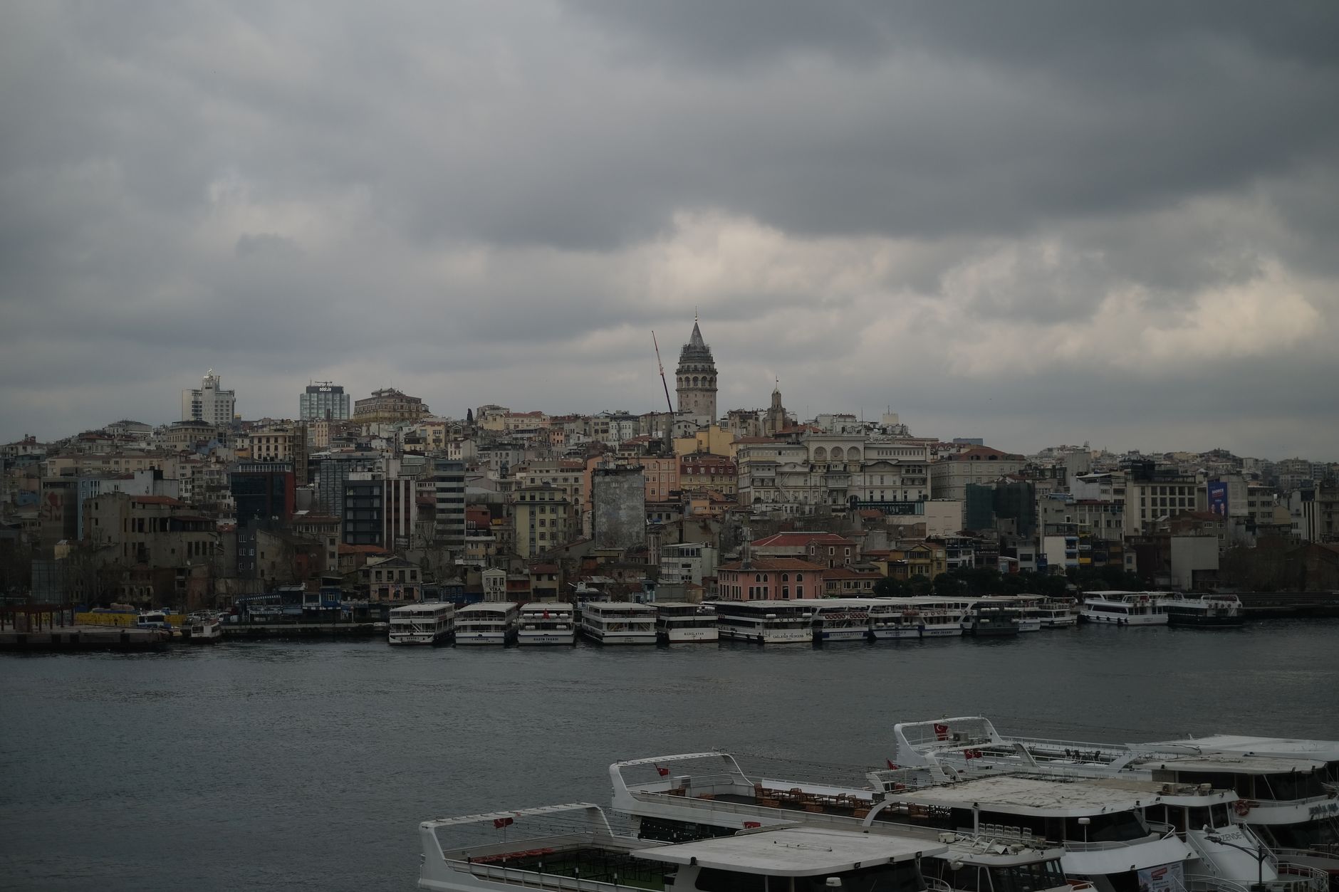 A cloudy day in Istanbul, showing the skyline with Galata Tower and boats on the water.