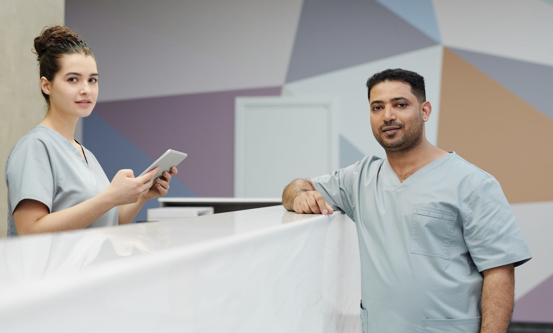Two healthcare professionals at a sleek clinic reception, one using a tablet.