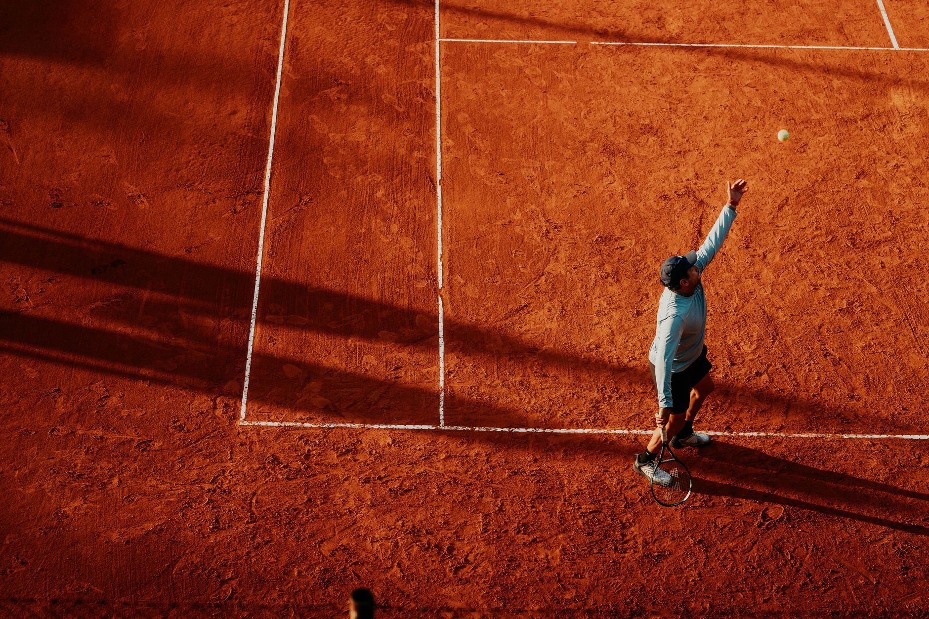 A tennis player in a blue shirt prepares to serve on a clay court.