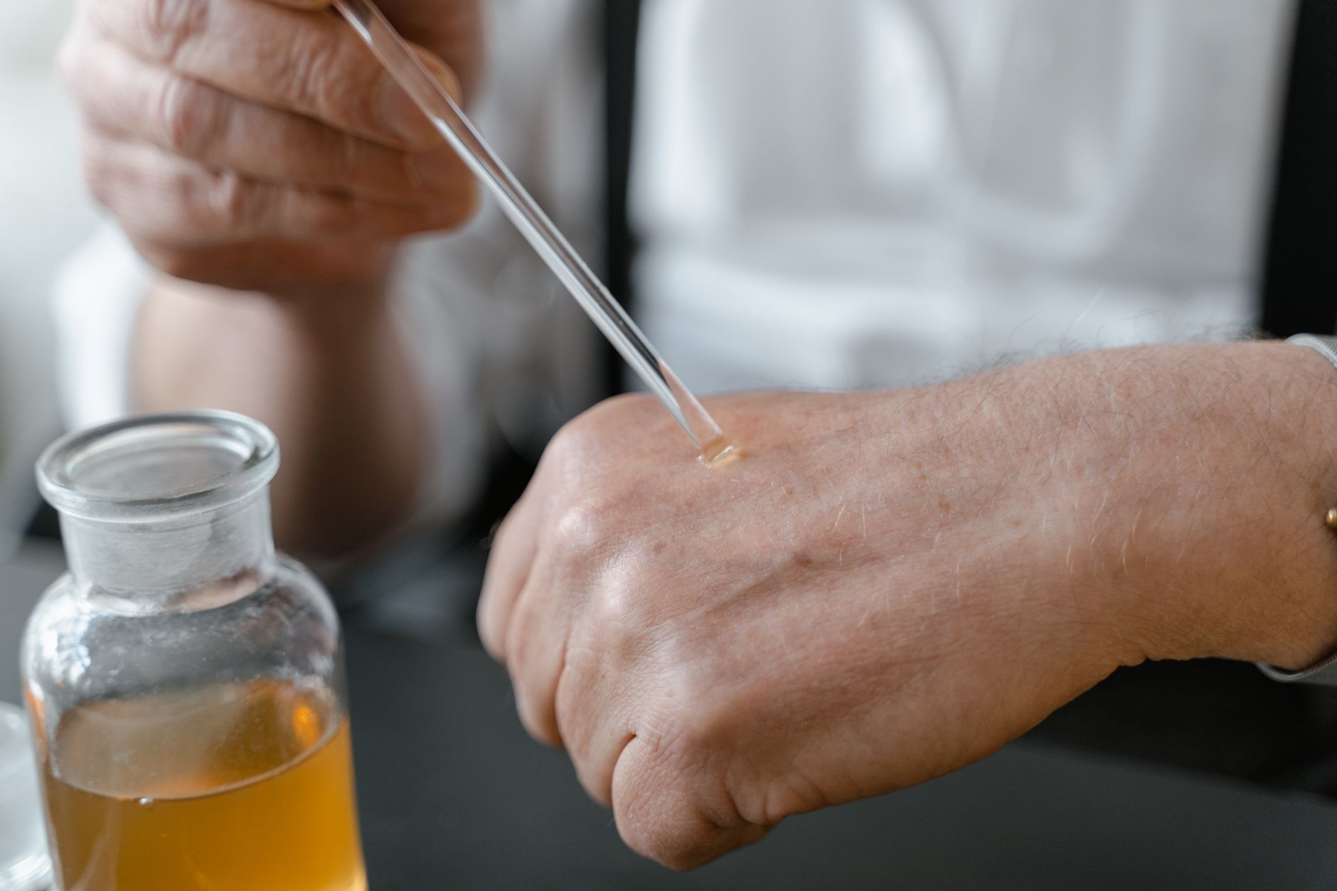 Close-up of a hand using a dropper to apply liquid on a patient's wrist.