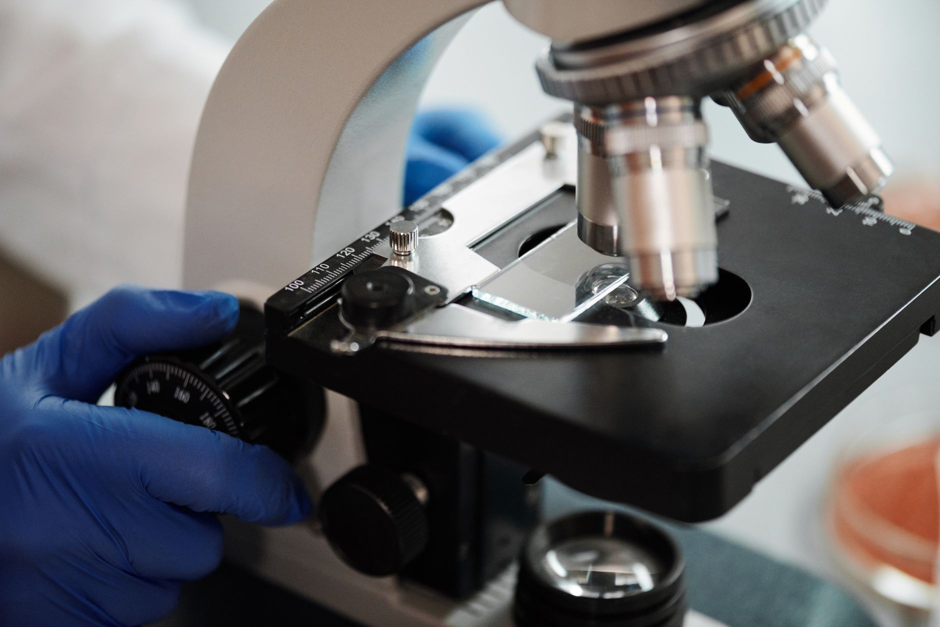Close-up of a microscope with a gloved hand adjusting the focus, used for pathology examination.